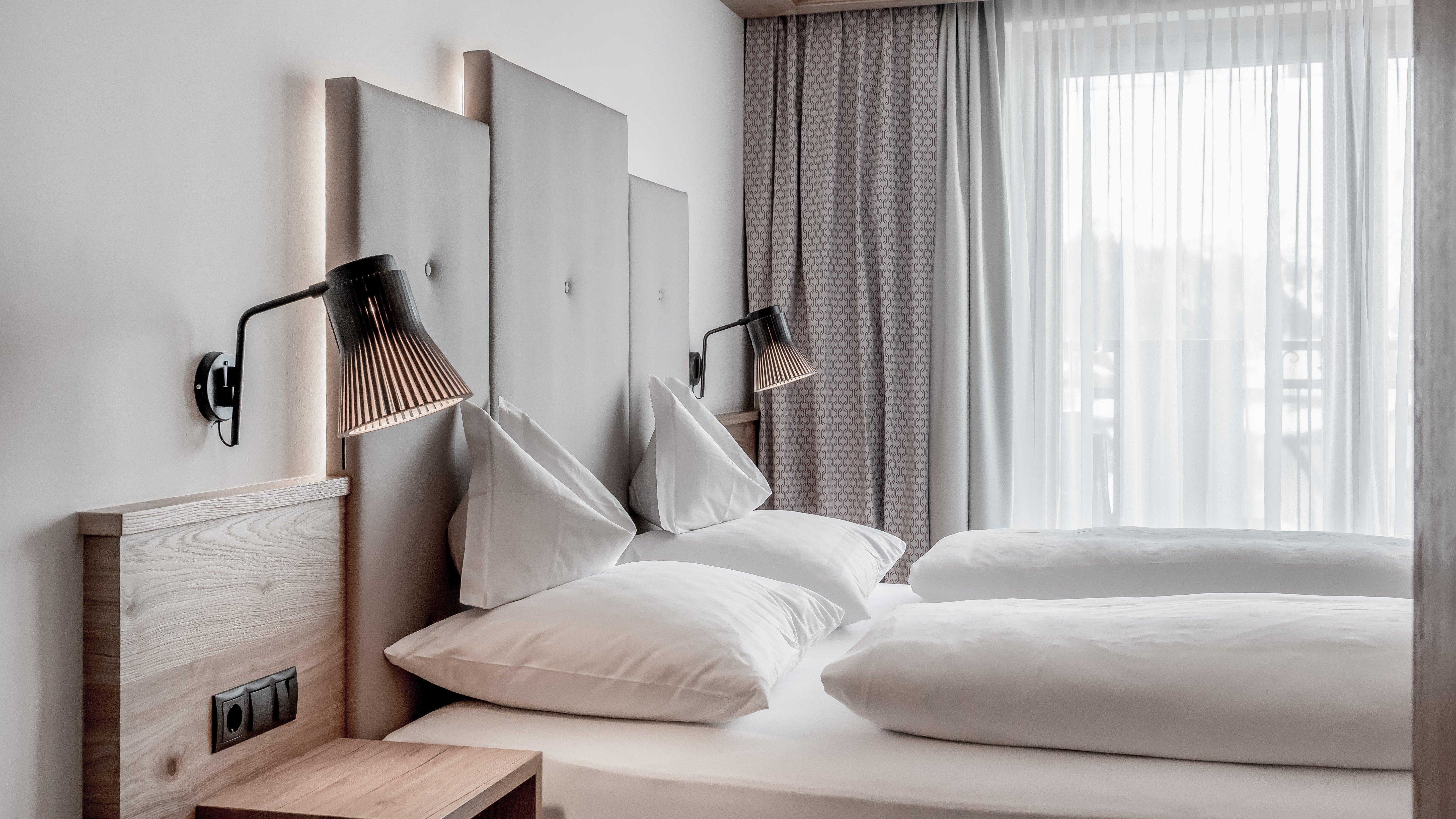 Minimalistisches Schlafzimmer mit zwei Betten, modernen Wandlampen und großen Fenstern