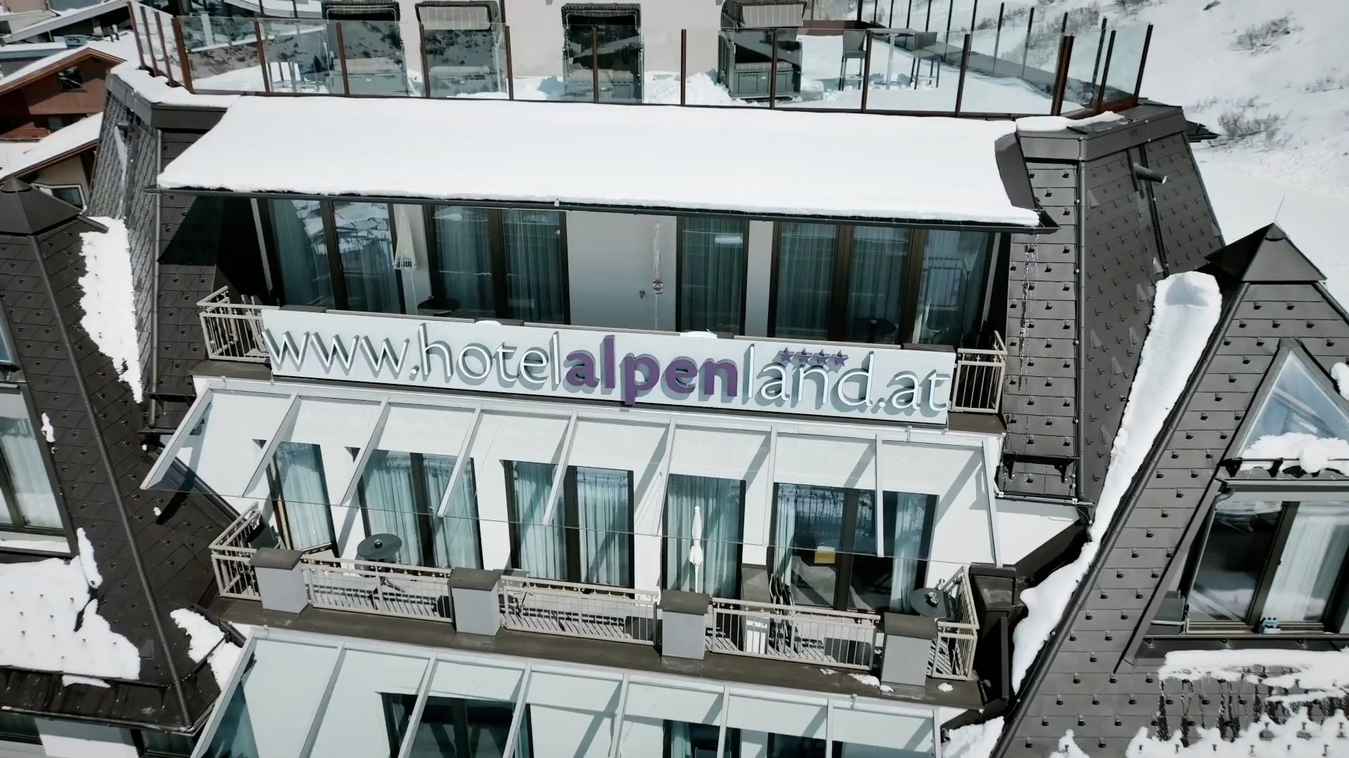 Ein modernes Hotelgebäude mit großen Glasfenstern und Schnee auf dem Dach in den Bergen.