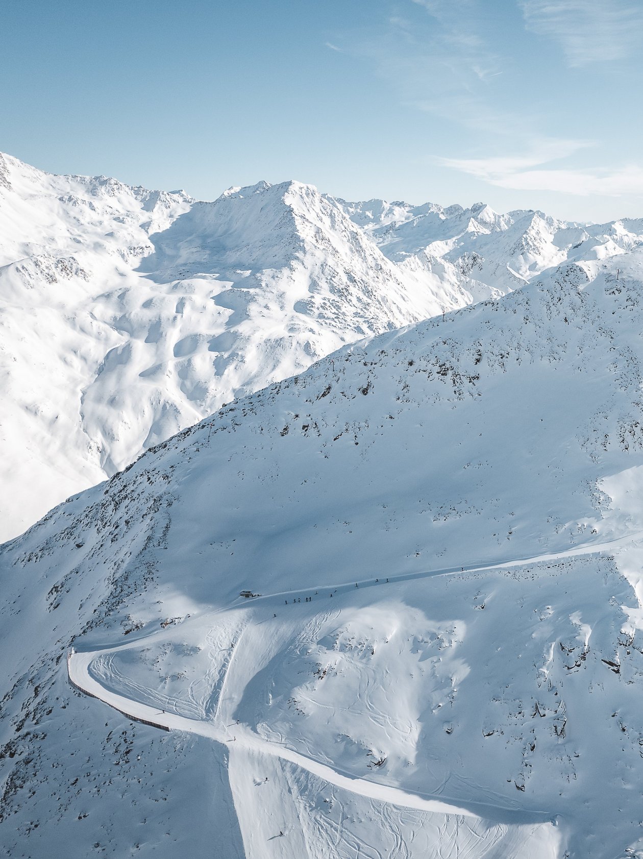 Luftaufnahme von schneebedeckten Bergen mit einer kurvenreichen Straße im Winter