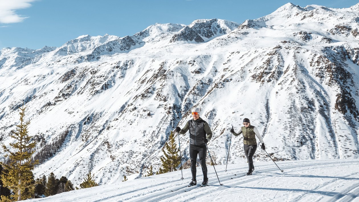 Skiabenteuer in den Alpen Zwei Personen fahren Ski auf einem schneebedeckten Gelände in den Bergen unter blauem Himmel