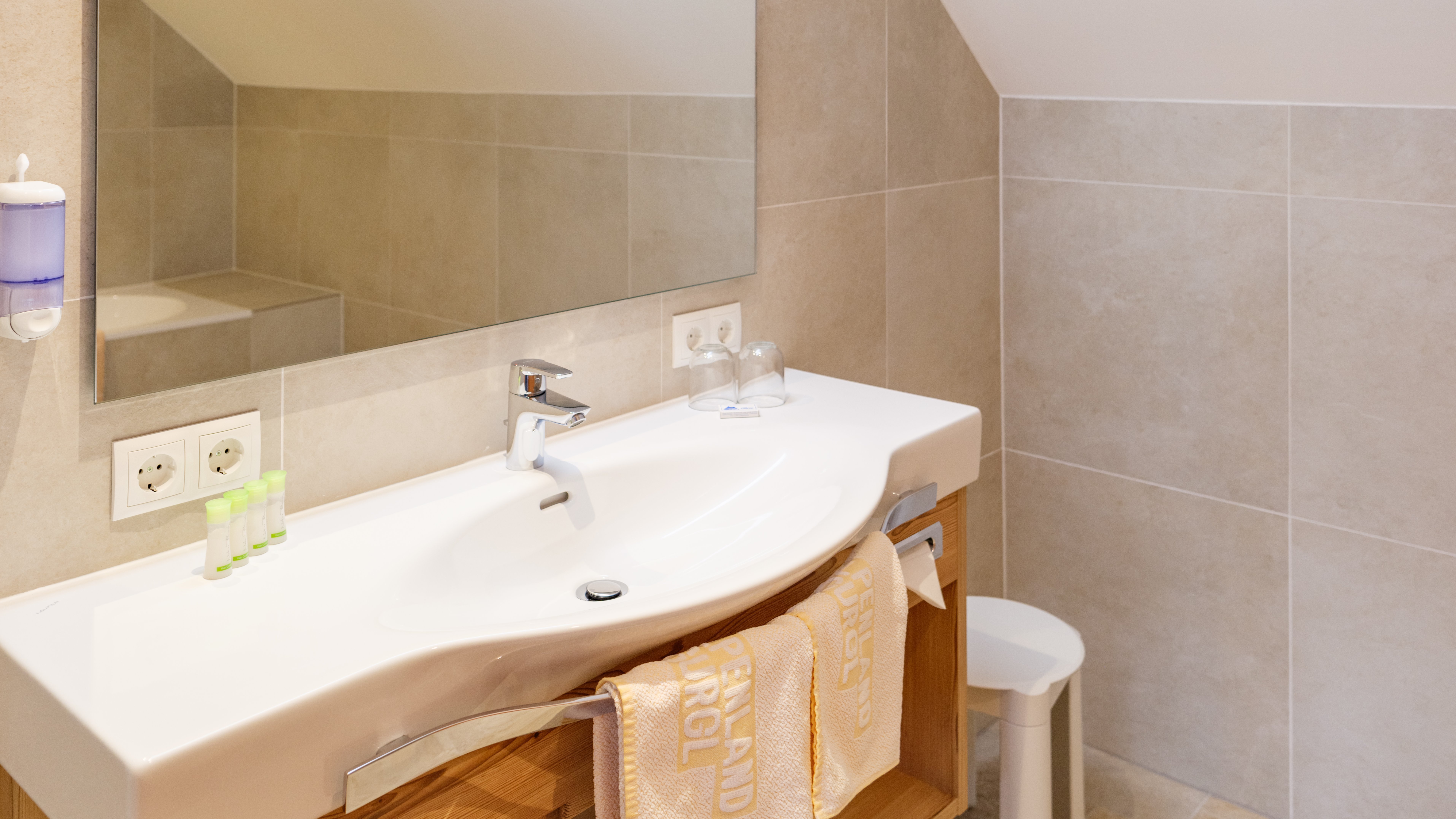 Modernes Badezimmer mit großem Spiegel, Waschbecken und Holzschränken auf neutralem Fliesenboden.