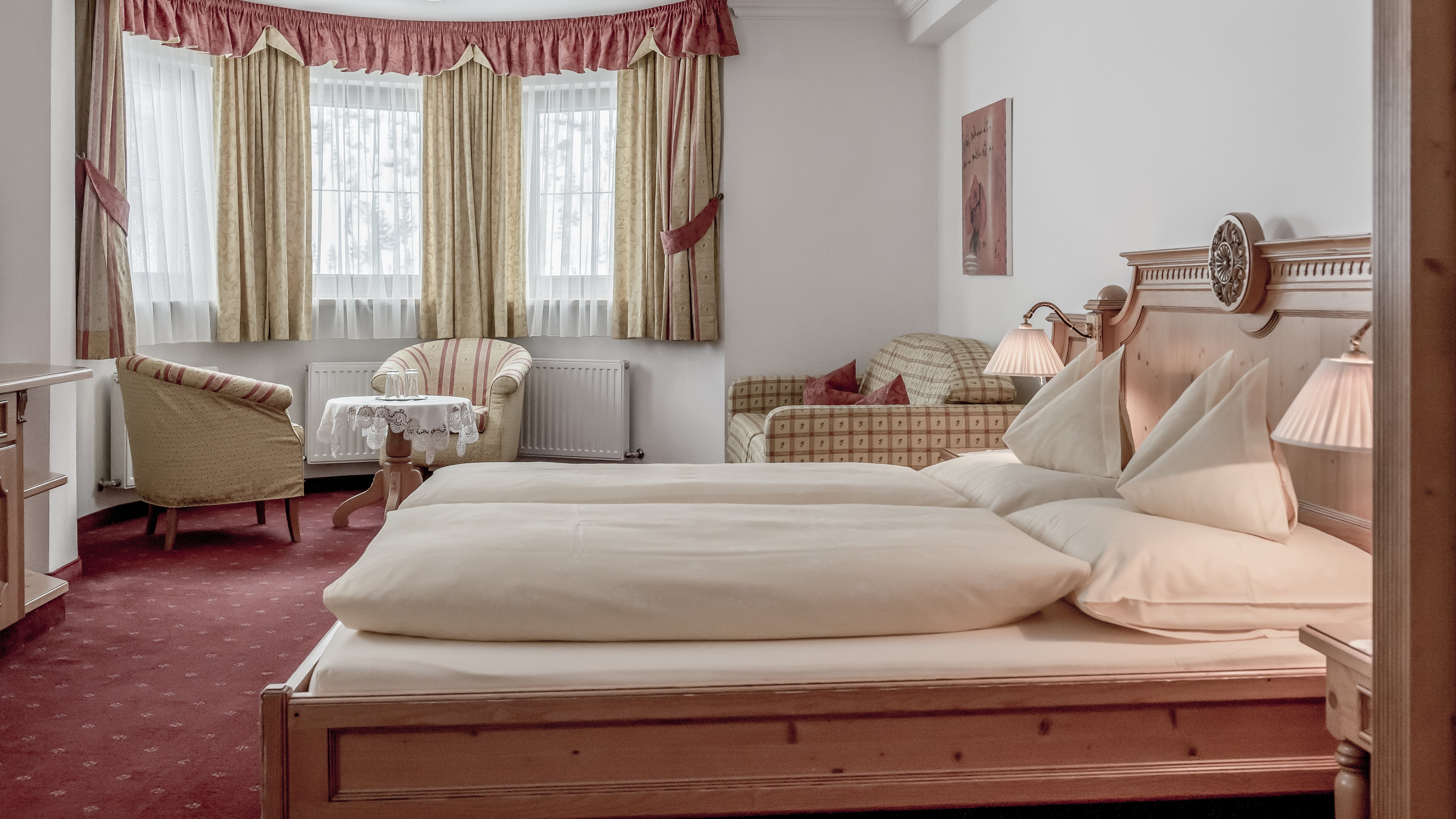 Gemütlicher Rückzugsort im Alpenland Helles Hotelzimmer mit Doppelbett, Couch und großen Fenstern mit Vorhängen zur natürlichen Beleuchtung.
