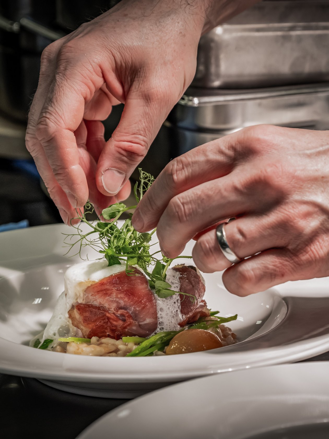 Kreative Präsentation der Gourmetküche Ein Koch garniert ein Gericht mit frischen Kräutern von Hand.