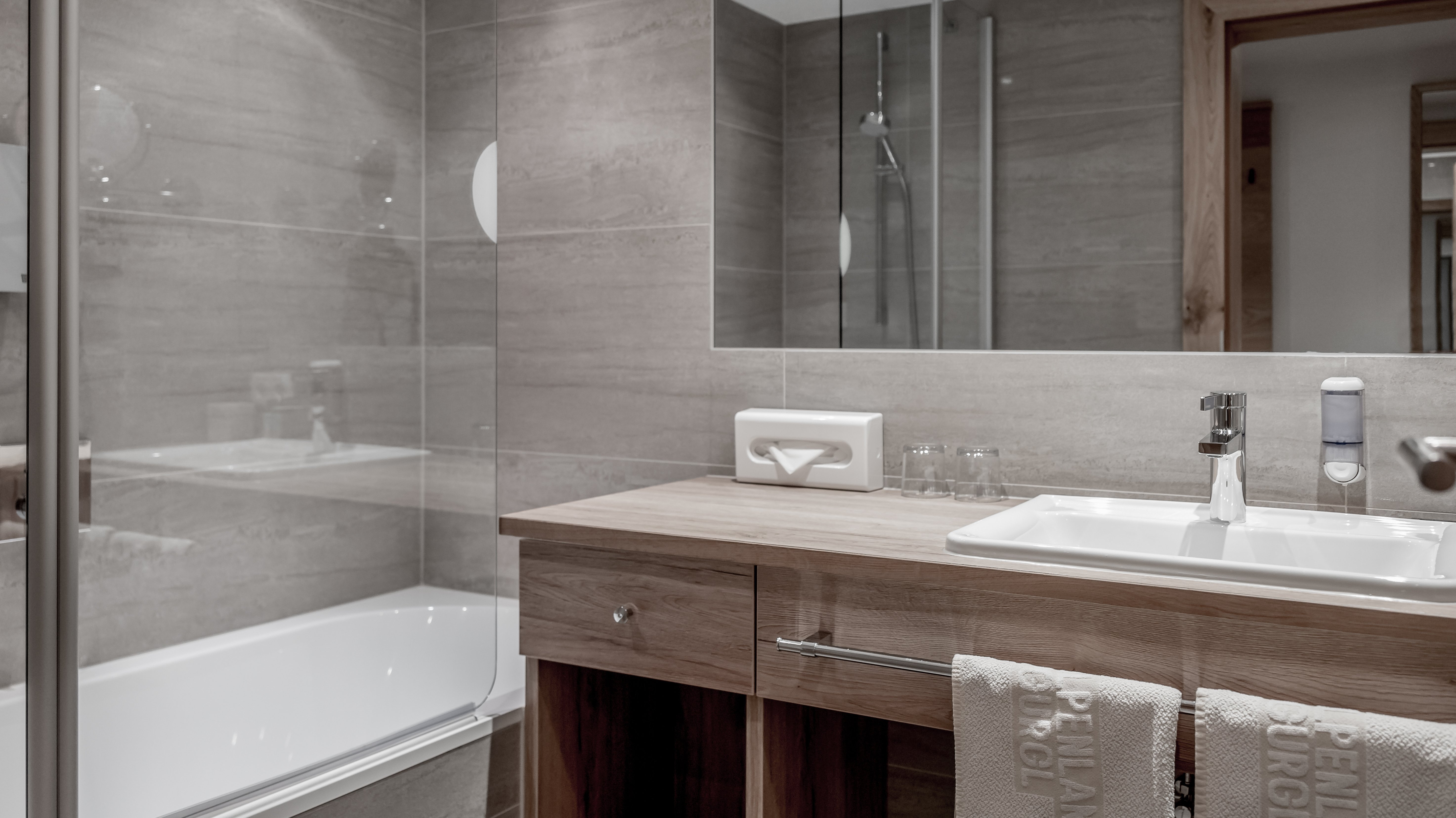 Modernes Badezimmer im Alpenland Badezimmer mit Glasdusche, Badewanne und Holzwaschtisch mit Spiegel in modernem Design.