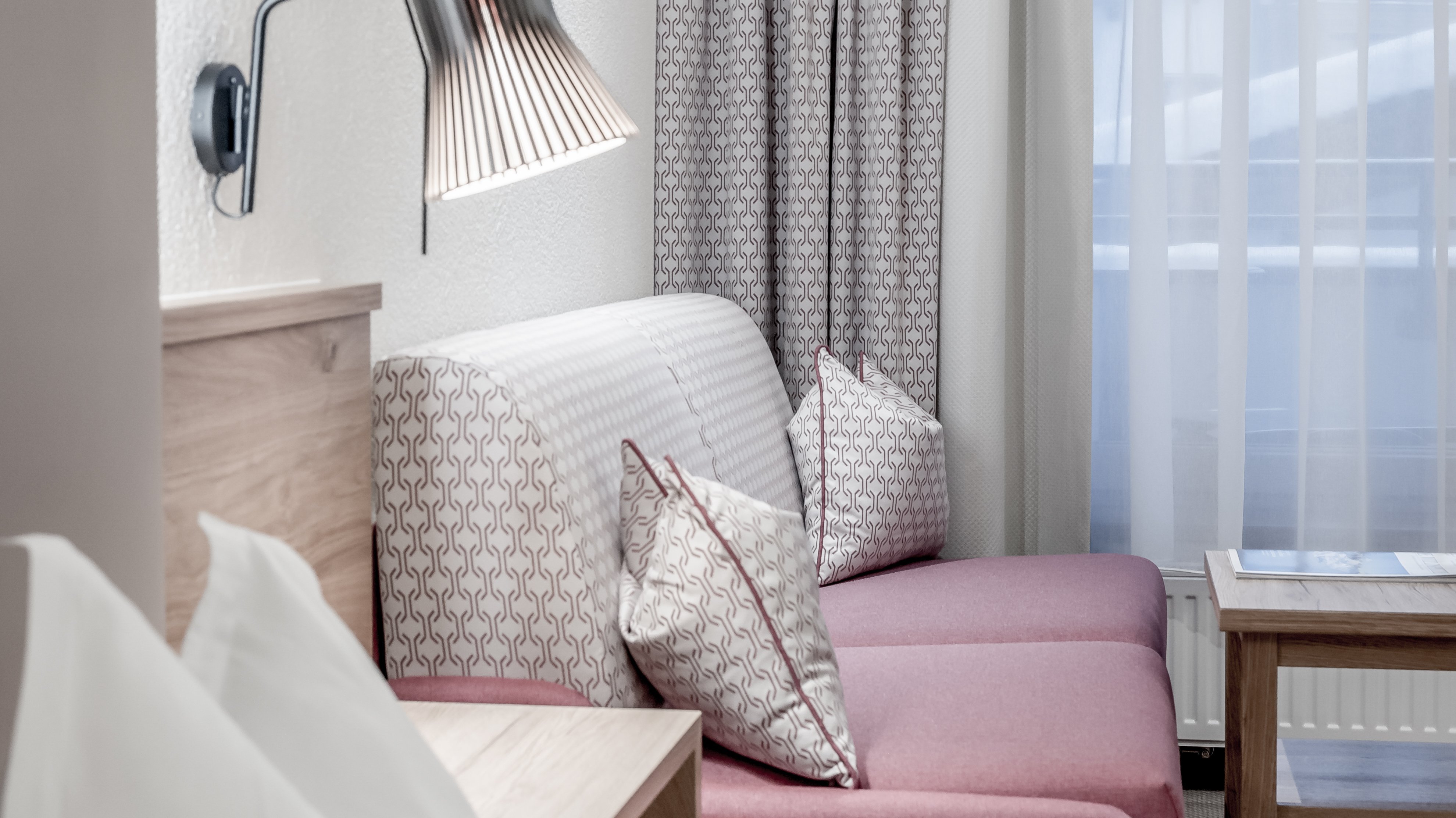 Moderne Eleganz im Hotelzimmer Helles Hotelzimmer mit Sofa, Dekokissen und stilvoller Lampe unter einem Fenster.