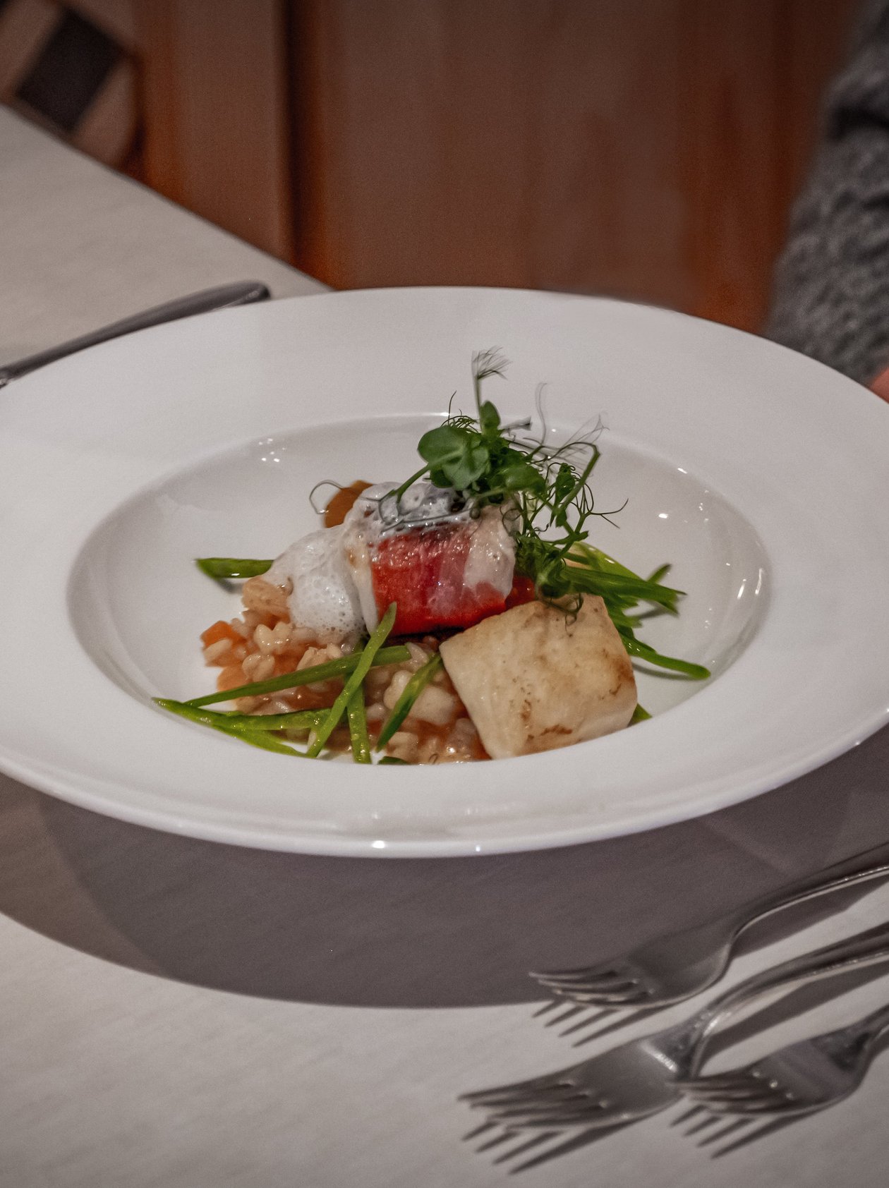 A finely plated gourmet dish served to a diner featuring various proteins and garnishes.