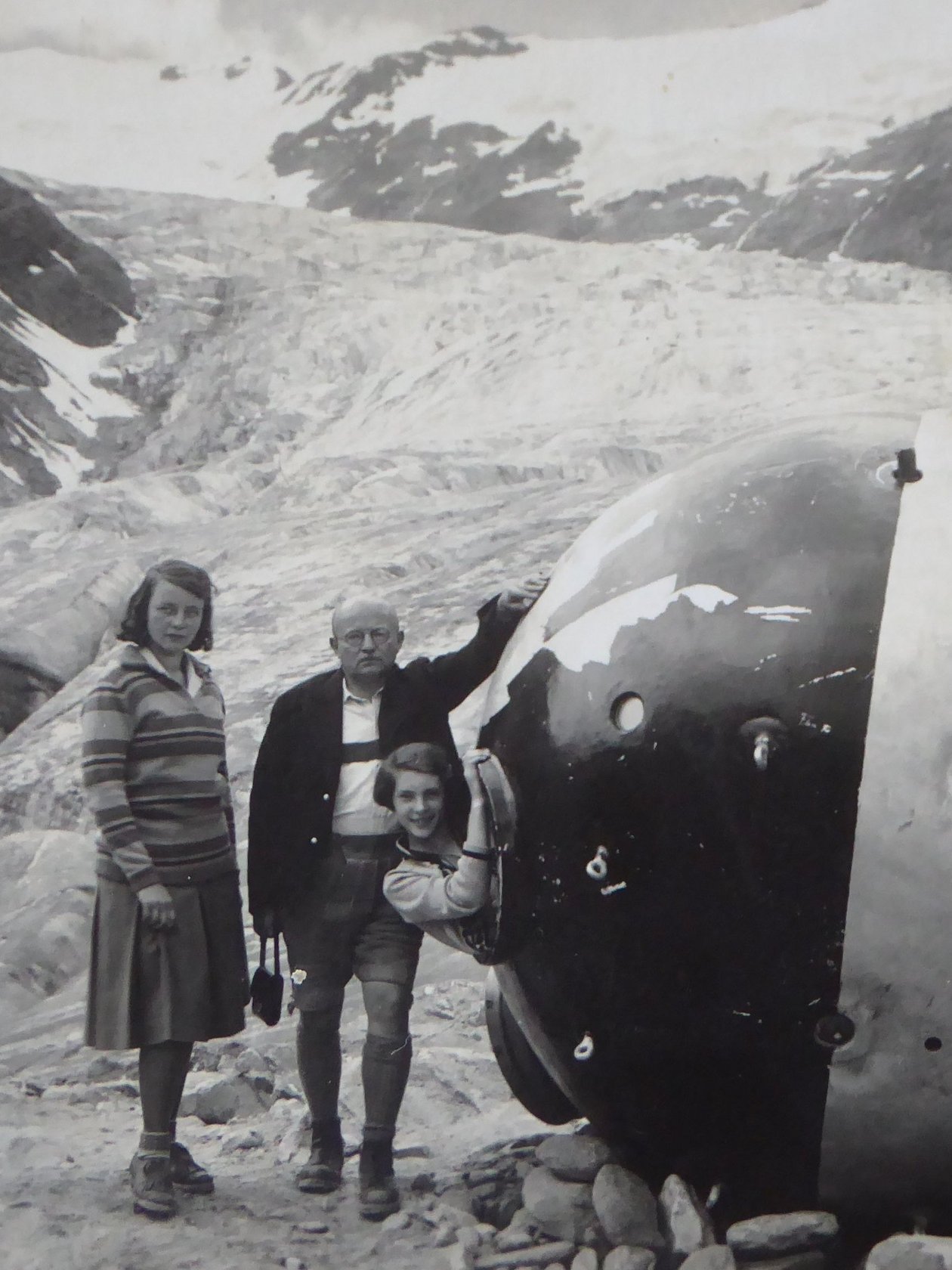Familie steht neben einer großen Kugel auf einem Gletscher in den Bergen, umgeben von einer beeindruckenden Landschaft.