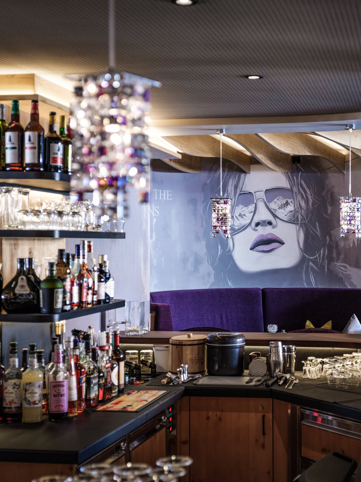 Moderne Bar im Alpenland Innenansicht einer stilvollen Bar mit einem großen Wandgemälde einer Frau mit Sonnenbrille und dekorativer Beleuchtung.