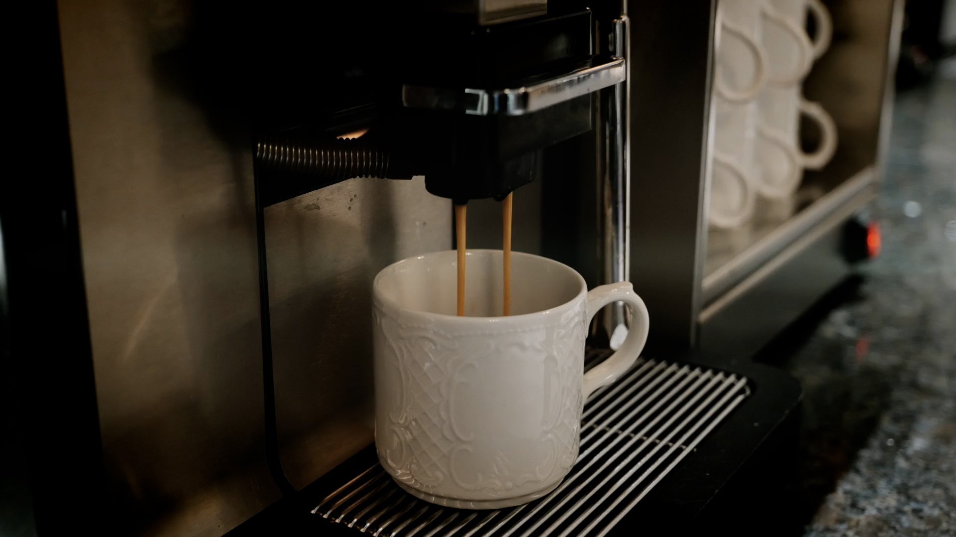 Frischer Espresso aus der Maschine Kaffeekanne mit frisch gebrühtem Espresso in weißer Tasse auf Tischplatte mit einem Handtuch.