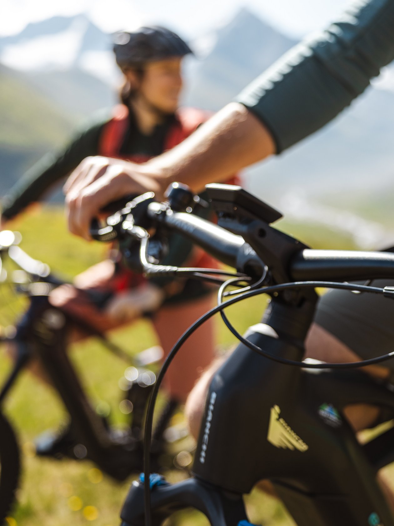 Nahaufnahme von den Händen eines Radfahrers an einem Mountainbike-Lenker, im Hintergrund ein weiterer Radfahrer.