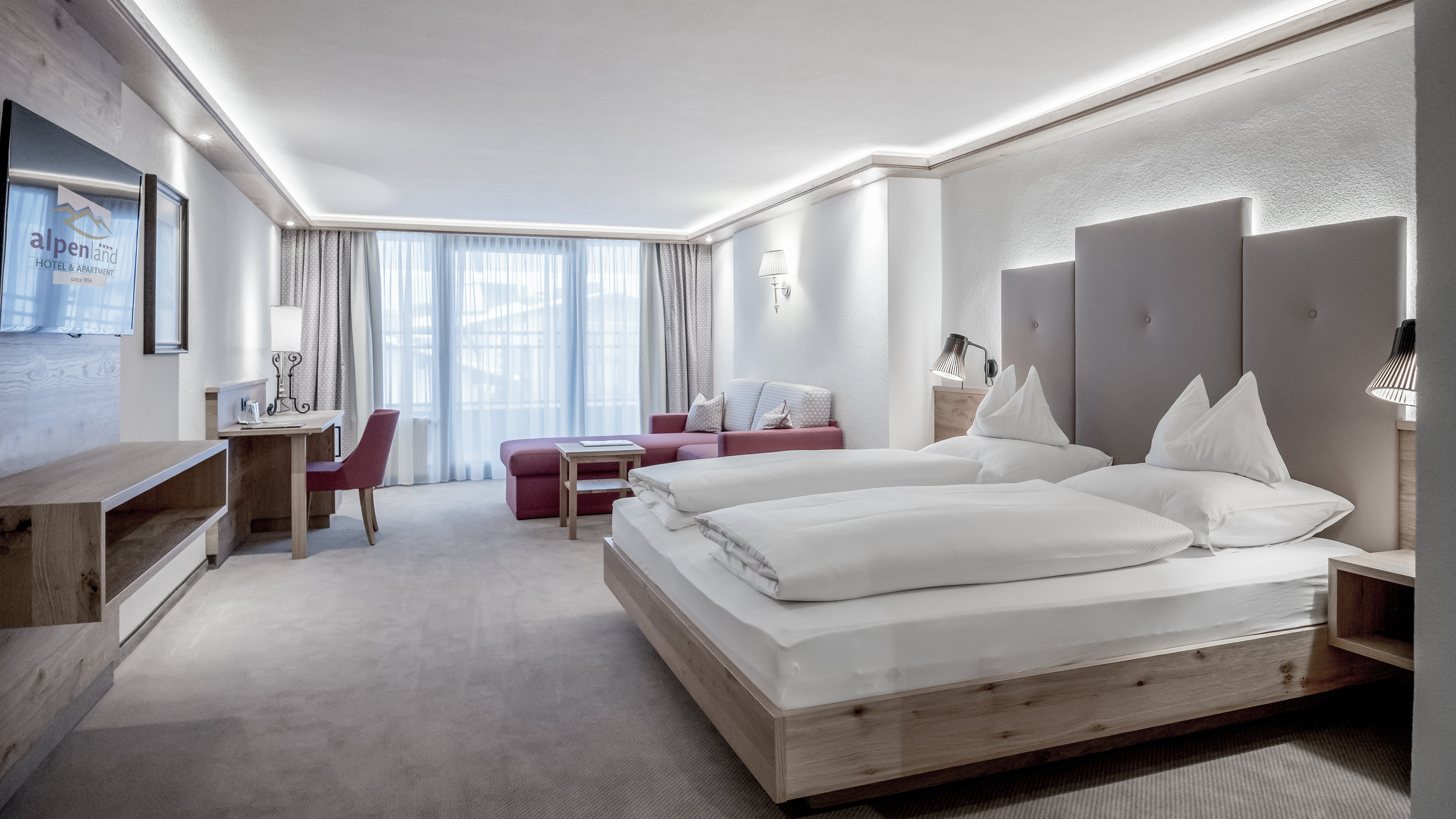 Moderne Hotelunterkunft im Alpenland Hotelzimmer mit Doppelbett, Sitzbereich und Schreibtisch, große Fenster für Tageslicht.