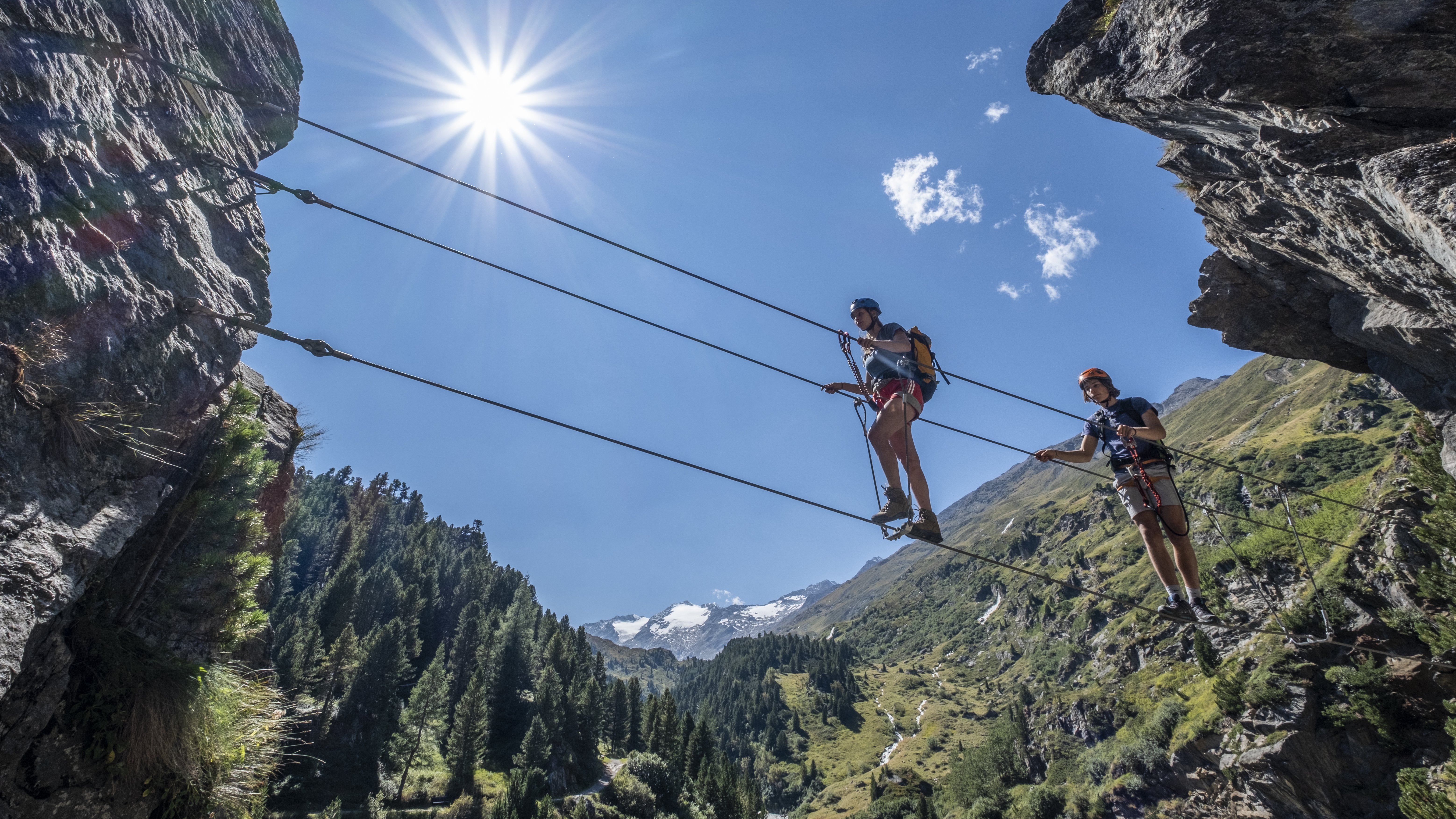 Zwei Personen überqueren eine Hängebrücke in den Bergen bei Sonnenschein im Freien.