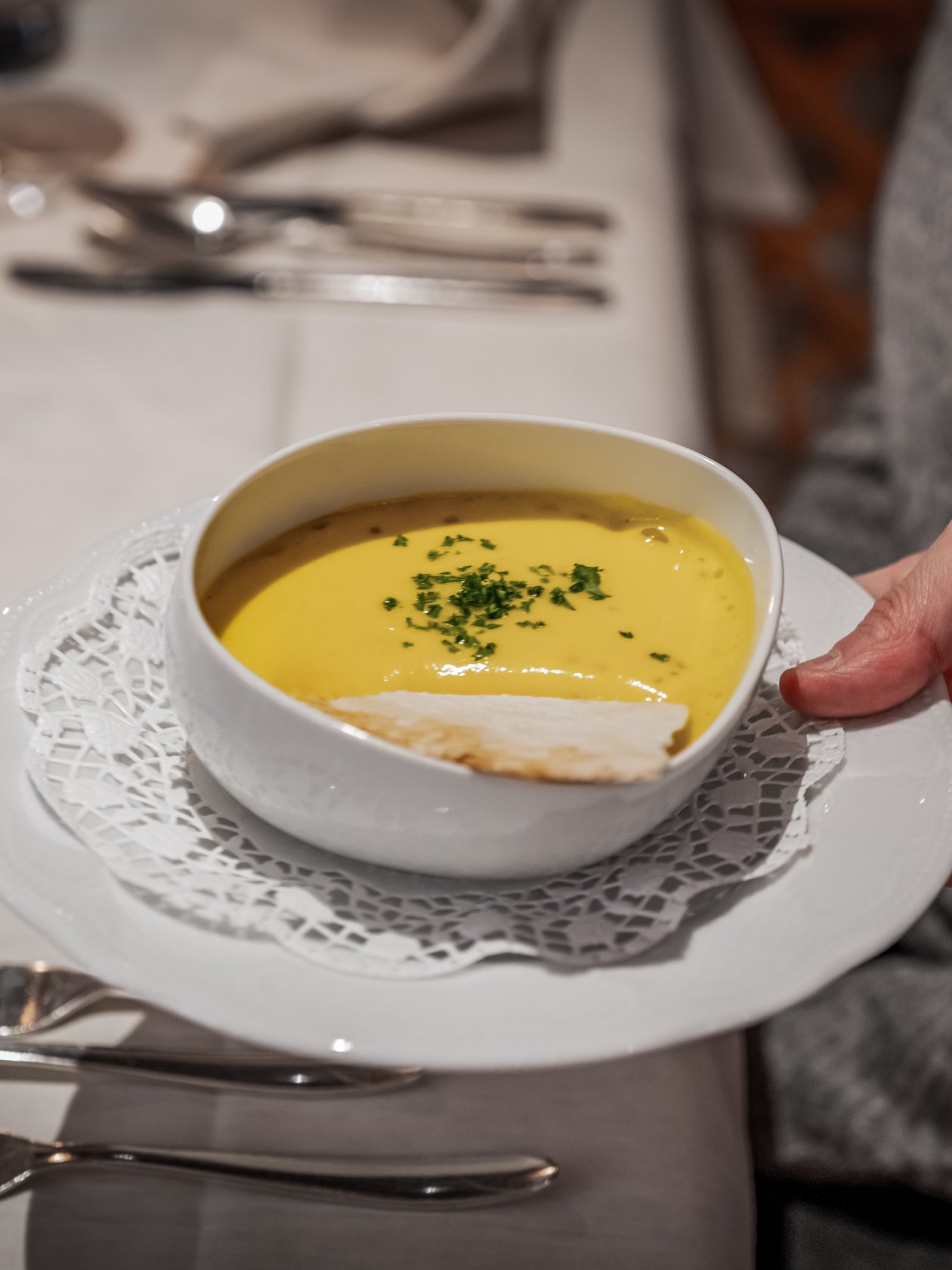 Kulinarische Köstlichkeit mit Suppe Ein Teller mit einer Schüssel Suppe, garniert mit Kräutern, auf einem Tisch mit Besteck.