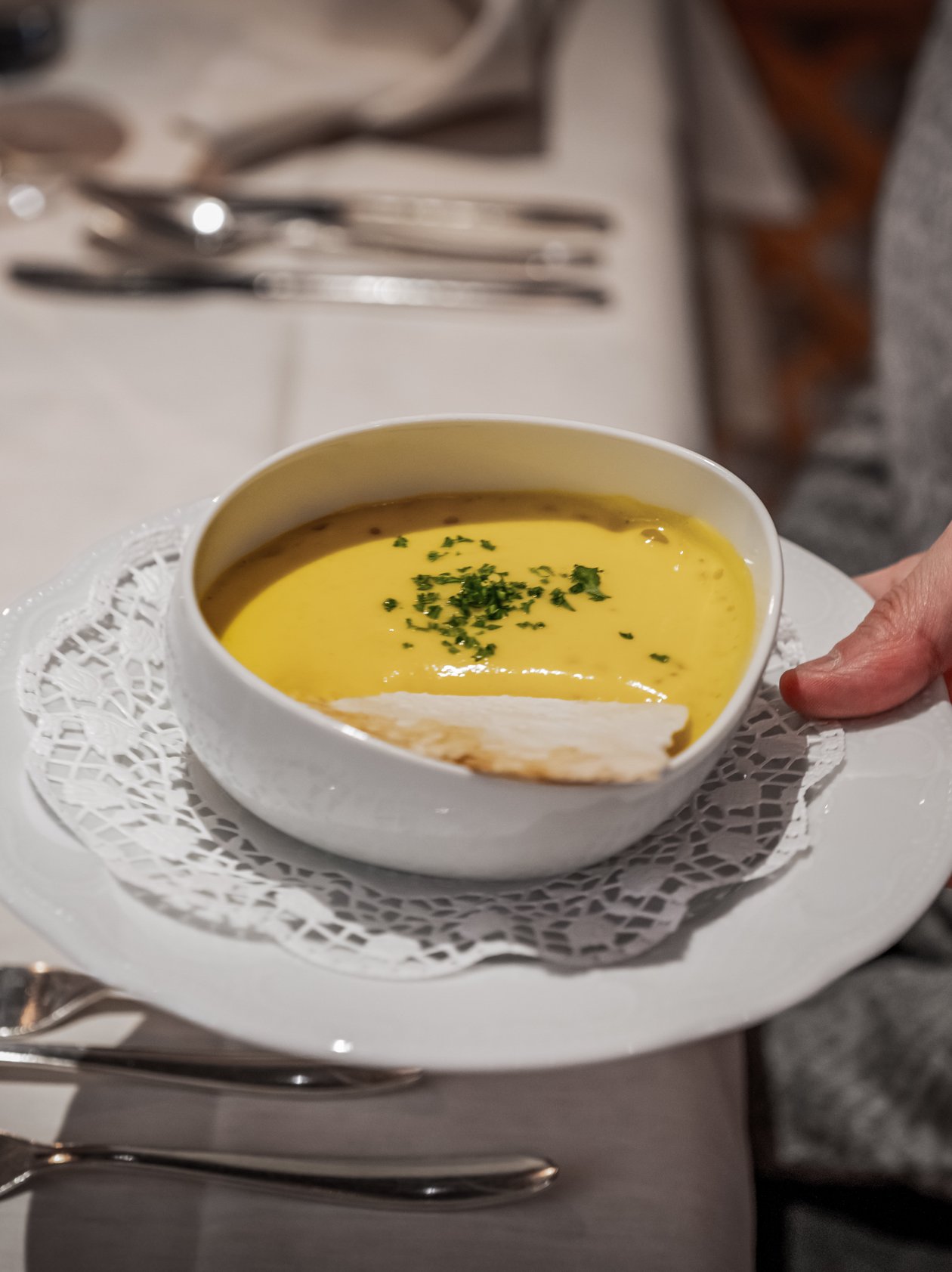 Kulinarische Köstlichkeit mit Suppe Ein Teller mit einer Schüssel Suppe, garniert mit Kräutern, auf einem Tisch mit Besteck.