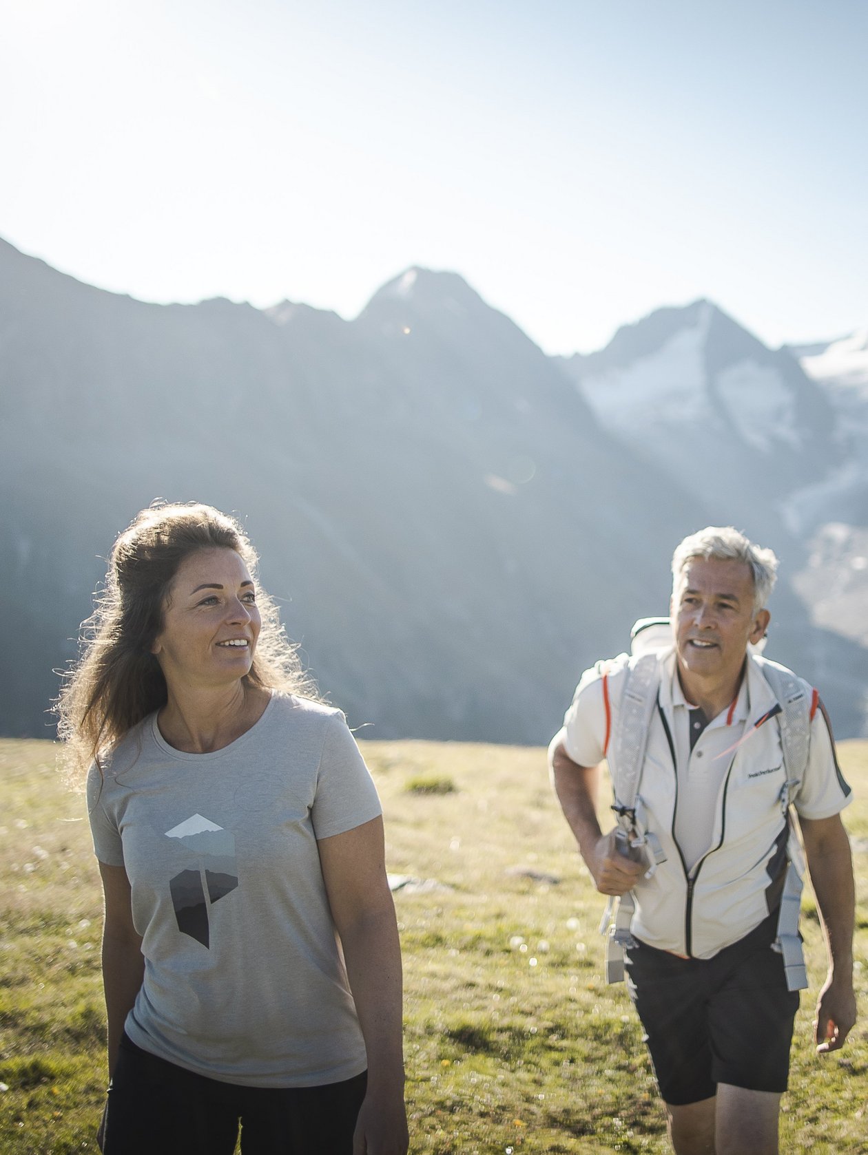A couple hiking on a trail through a mountainous landscape under a clear sky with trees around