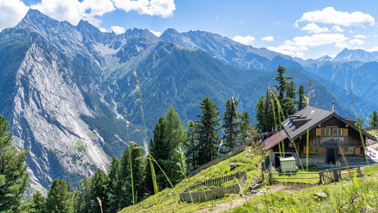 A cozy wooden cabin surrounded by greenery and mountains under a clear blue sky.
