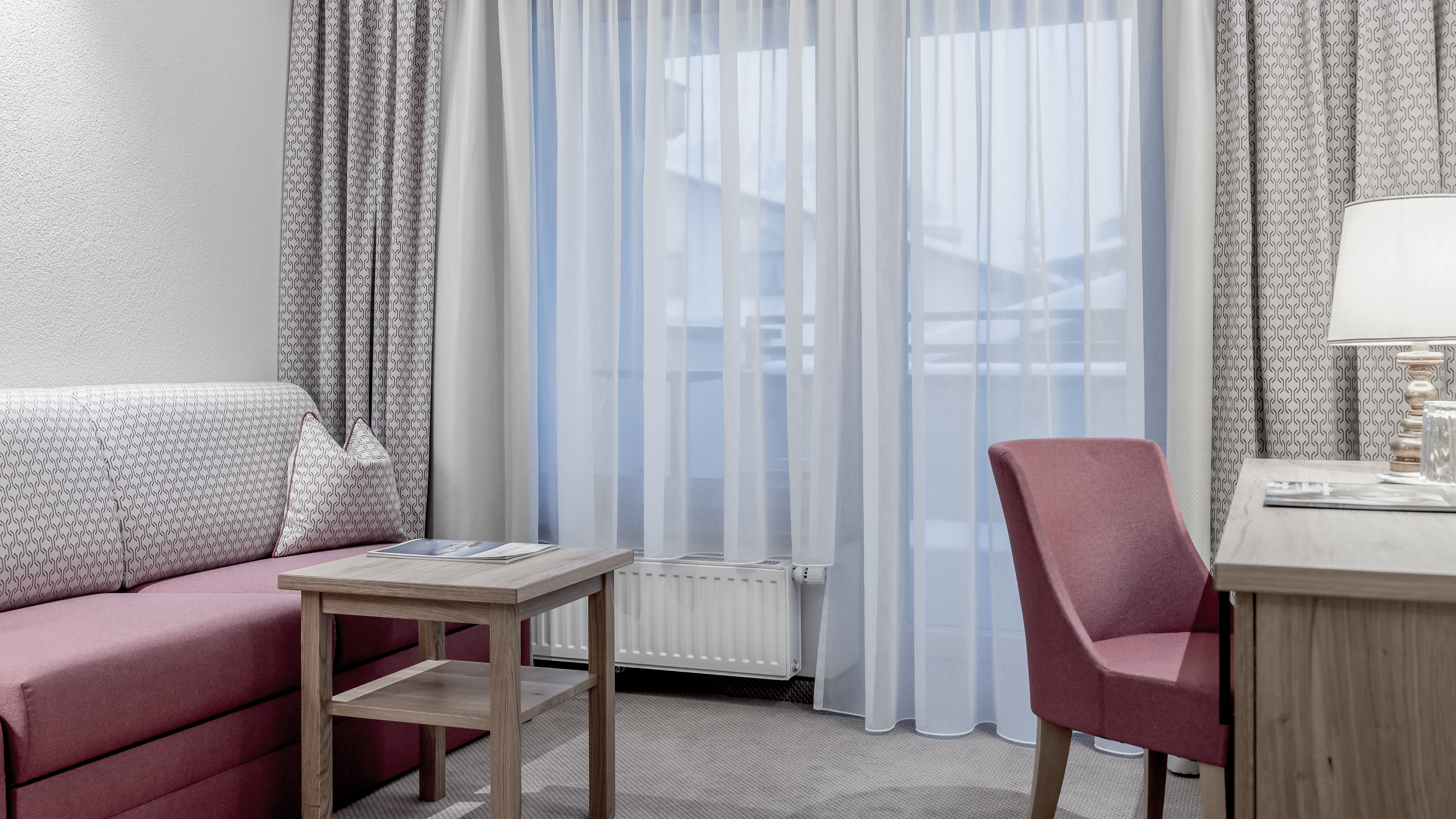 Modernes Hotelzimmer mit elegantem Design Hotelzimmer mit pinkem Sofa, Holztisch und Schreibtischlampe, lichtdurchlässigen Vorhängen.