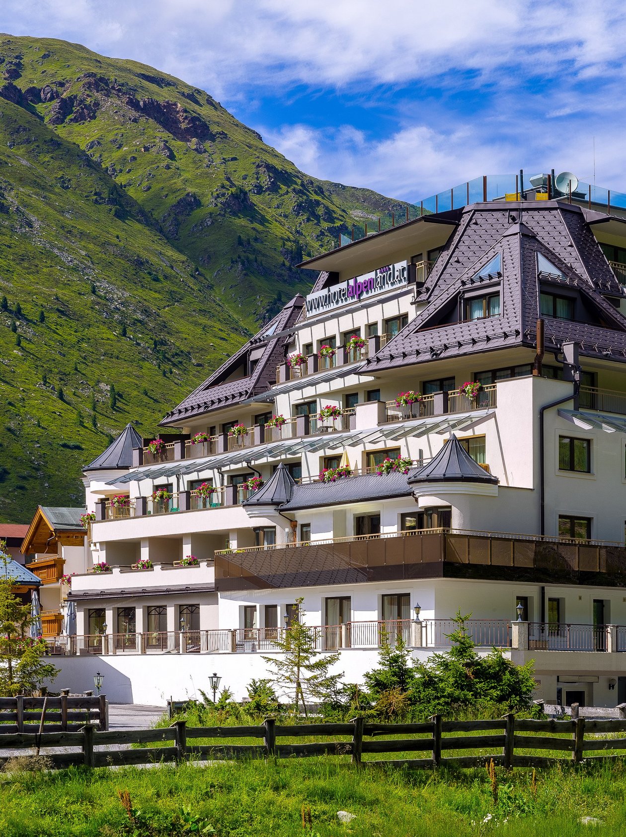 Mehrstöckiges Hotelgebäude vor grünen Bergen und blauem Himmel in den Alpen von Gurgl.