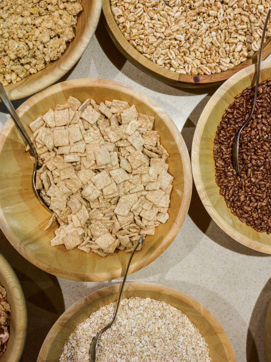 Verschiedene Cerealien in Holzschalen, darunter Haferflocken und Granola für ein gesundes Frühstück.