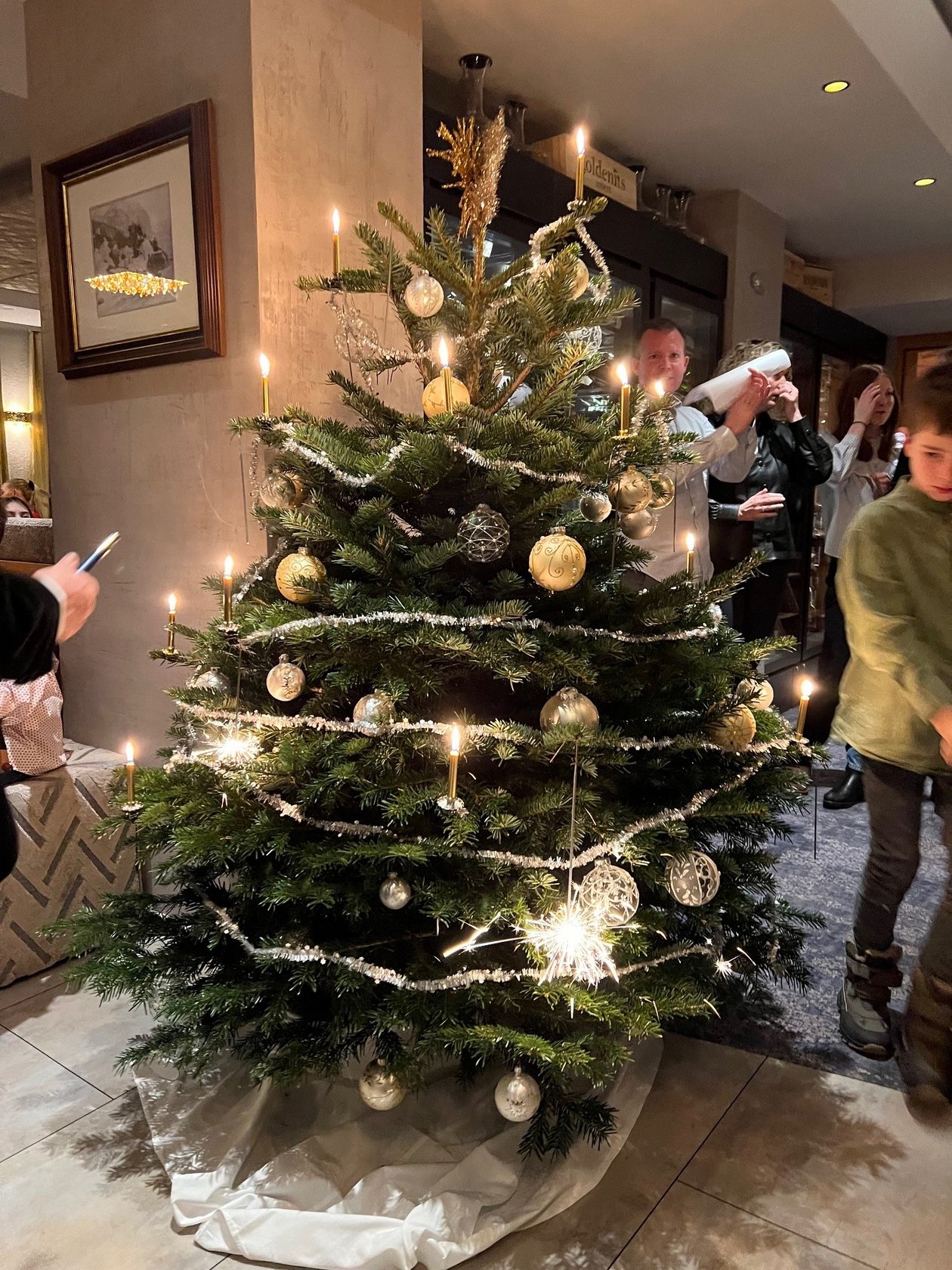 Dekorierter Weihnachtsbaum mit Kerzen und bunten Ornamenten in einem gemütlichen Raum.