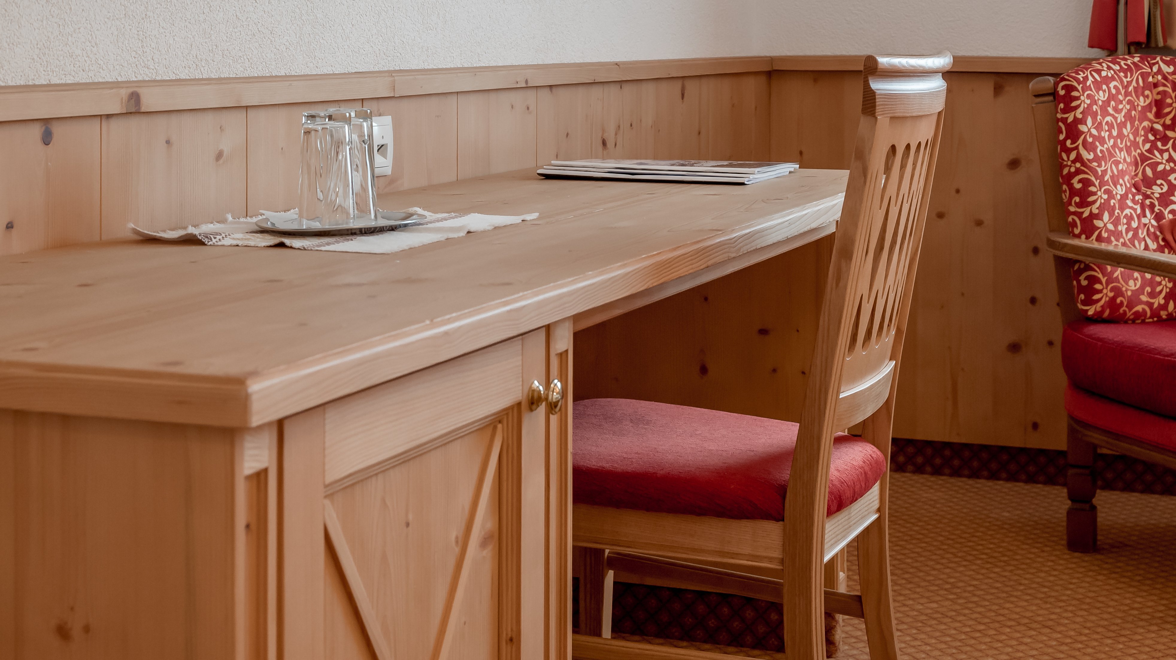 Moderne Zimmergestaltung im Hotel Alpenland Hotelzimmer mit Holztisch, Stuhl und Wandfernseher im Innenraum gesehen von vorne.