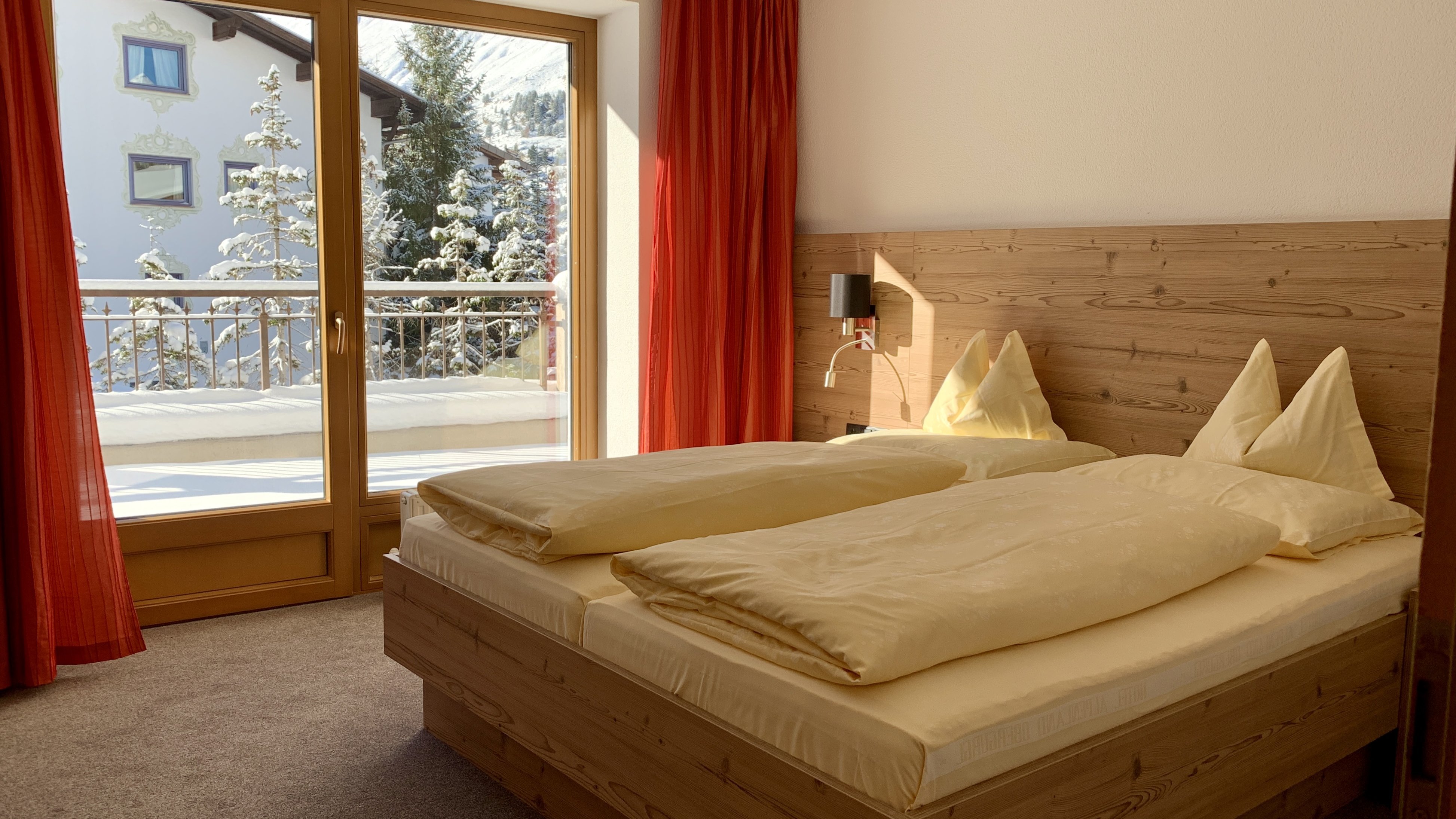 Schlafzimmer mit Holzmöbeln, großen Fenstern und Blick auf verschneite Bäume im Freien.