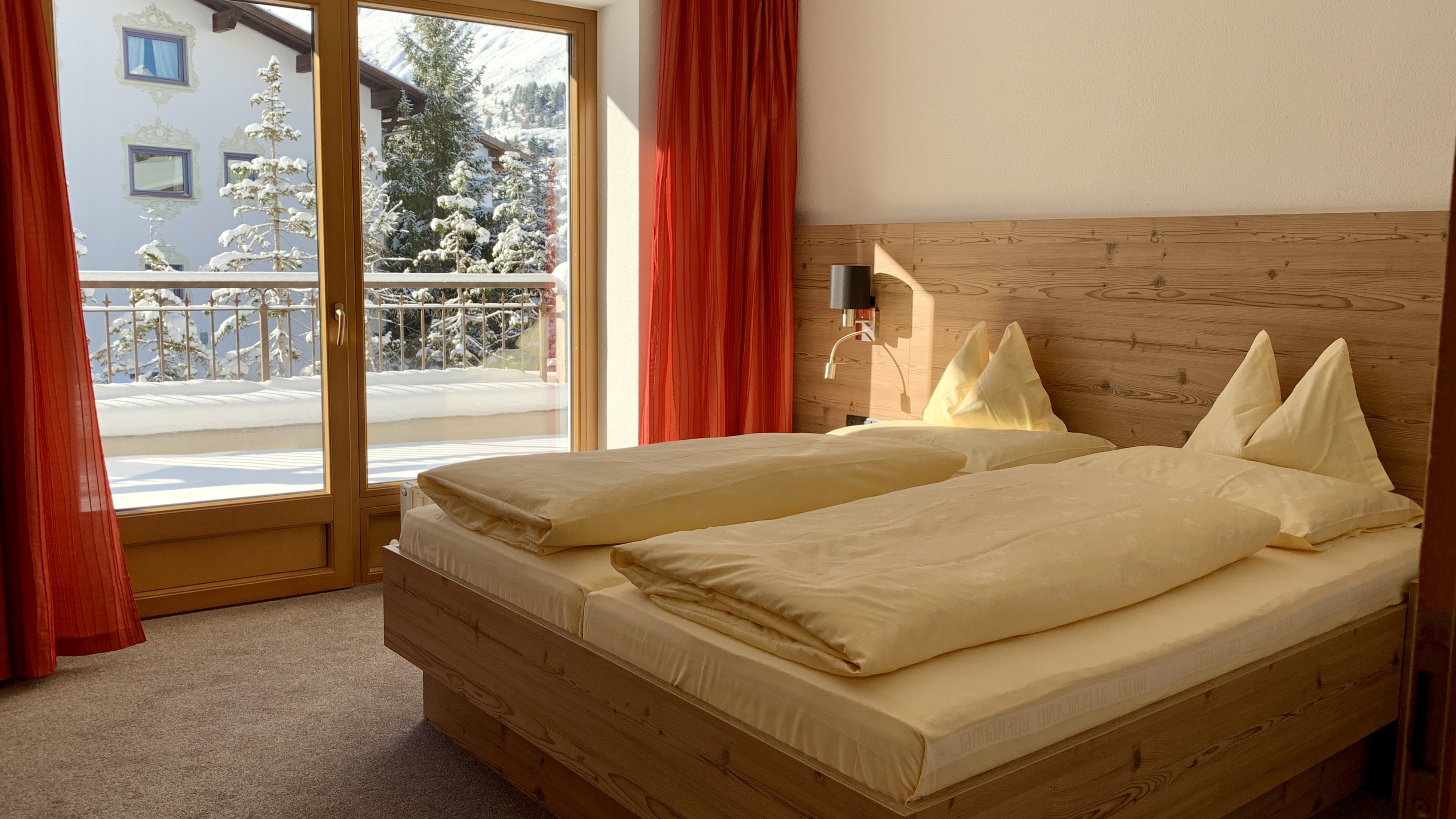 Gemütliches Schlafzimmer mit Bergblick Schlafzimmer mit Holzmöbeln, großen Fenstern und Blick auf verschneite Bäume im Freien.
