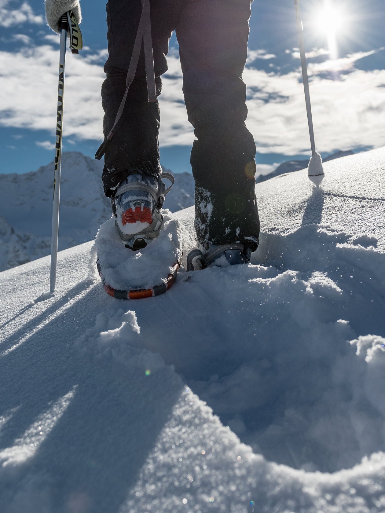 Eine Person geht mit Schneeschuhen durch den Schnee in einer Berglandschaft unter blauem Himmel.
