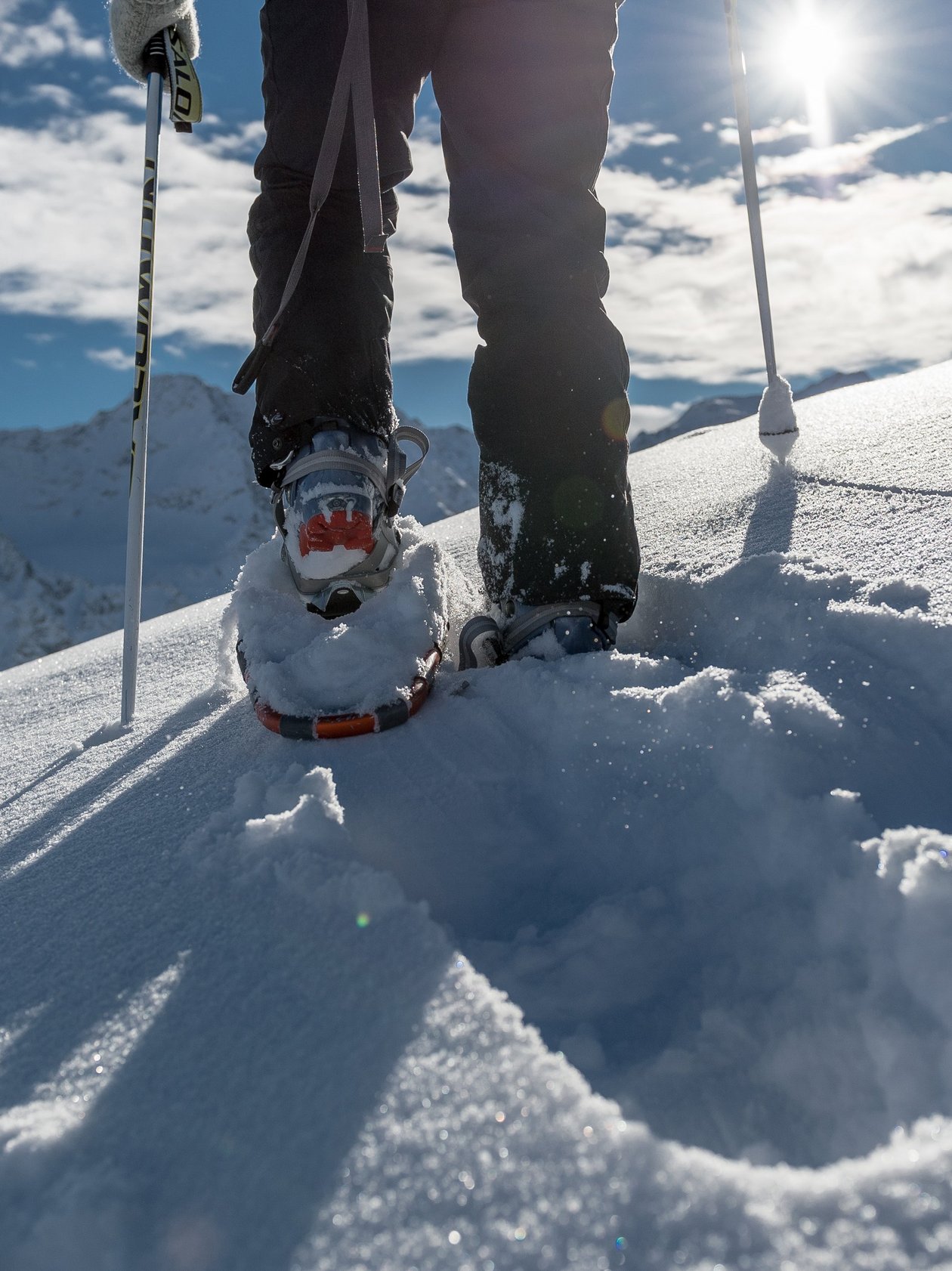 Explore Winter Trails with Snowshoeing Person snowshoeing on a snowy mountain trail under bright sun with peaks in the background
