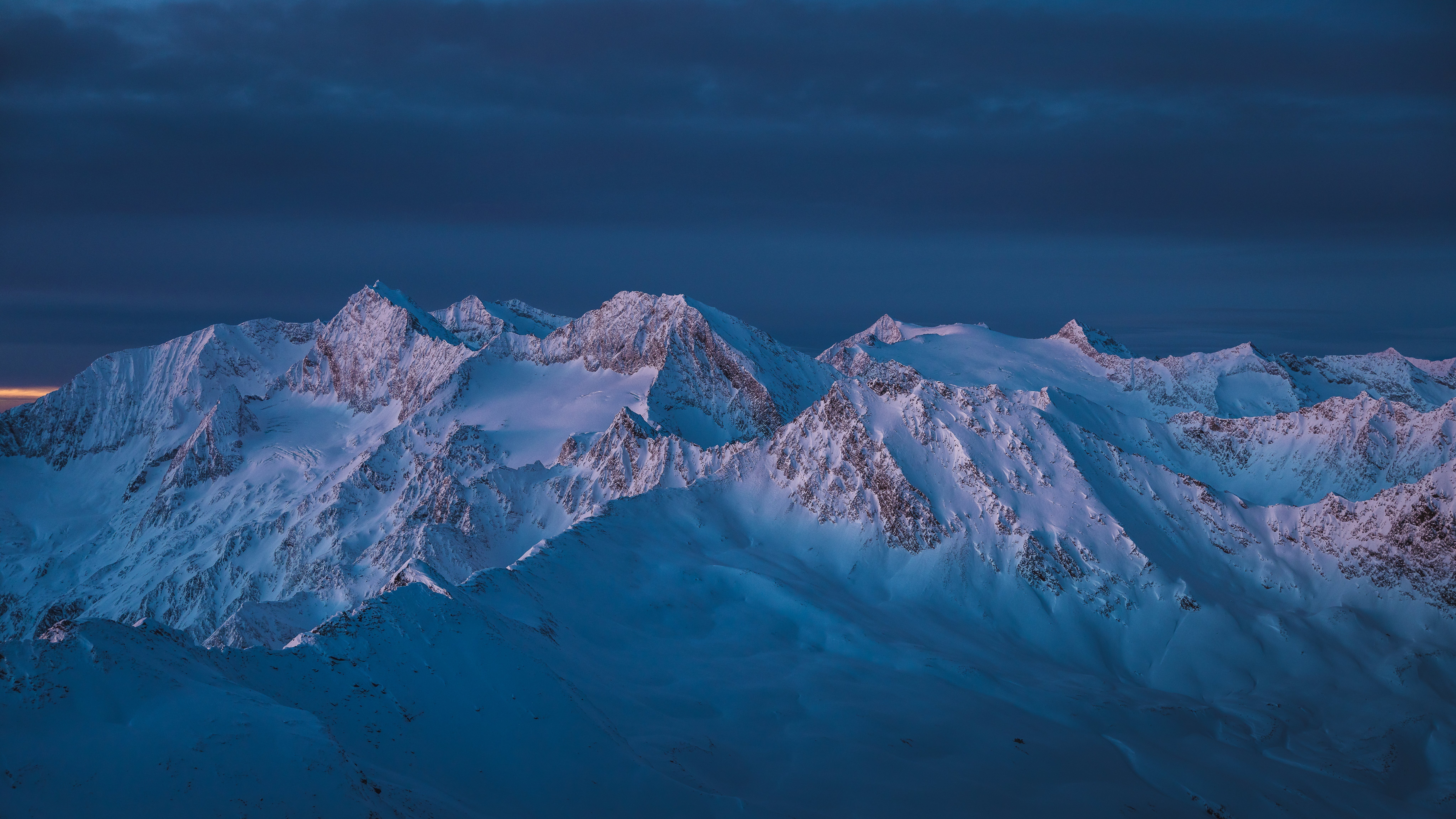 Schneebedeckte Berglandschaft unter einem Abendhimmel mit orangefarbenen und blauen Tönen.