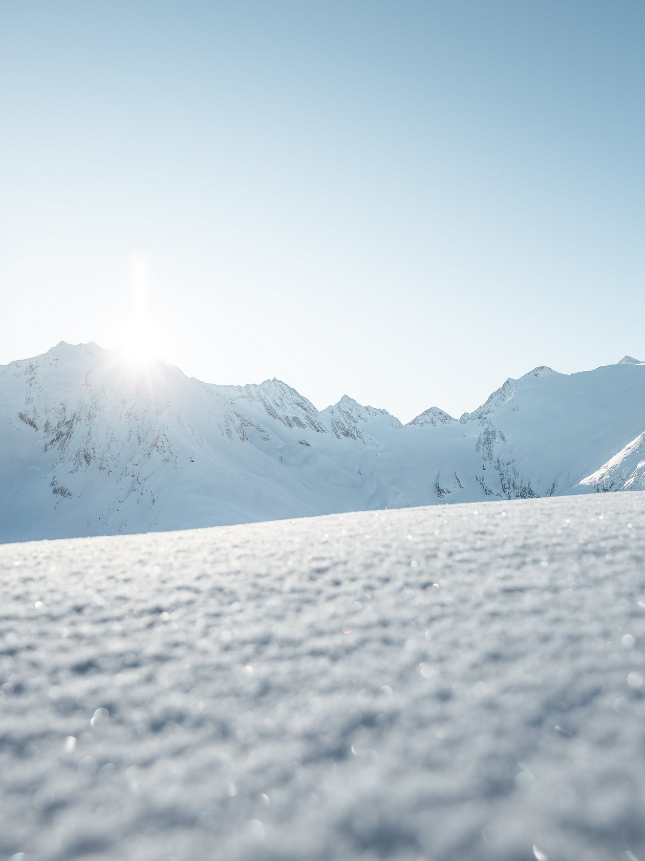 Schneebedeckte Berge unter klarem Himmel mit Sonnenaufgang im Hintergrund in den Alpen