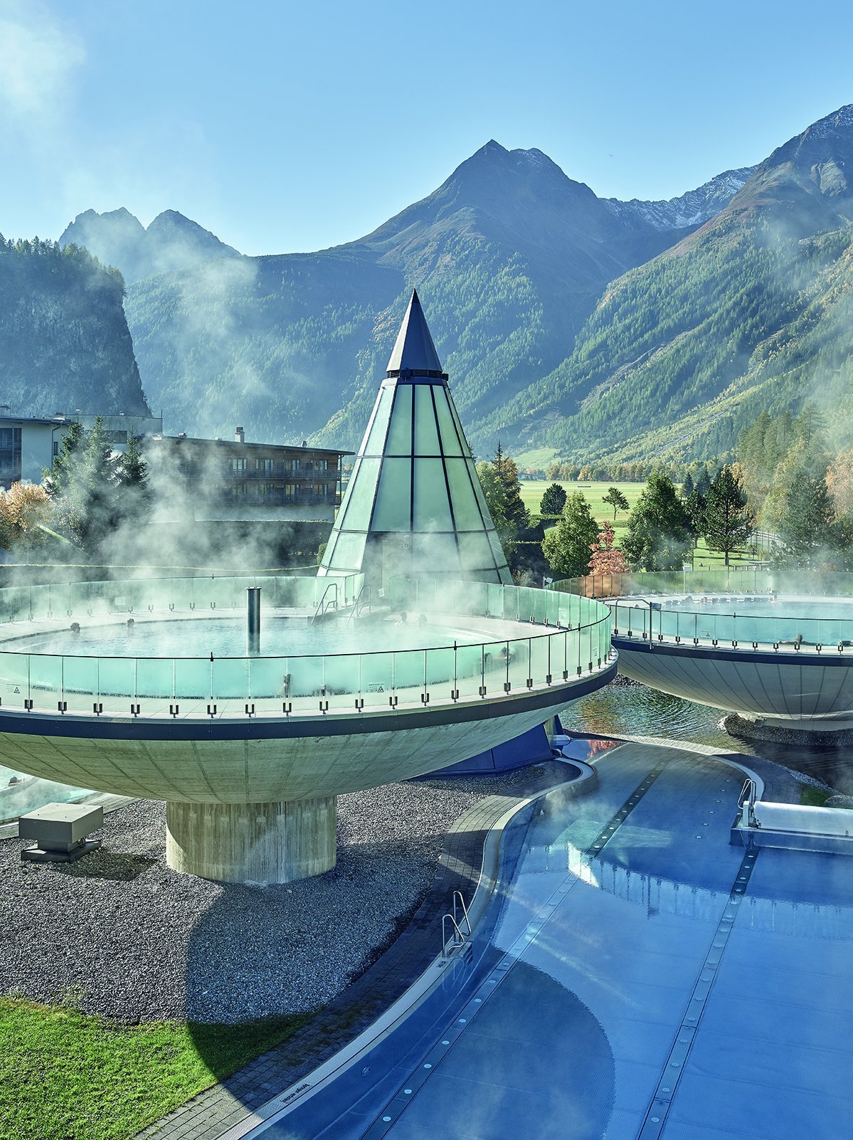 Moderne Therme im Alpenland Kreisförmige Thermalbecken und ein Außenpool in Berglandschaft mit klarem Himmel