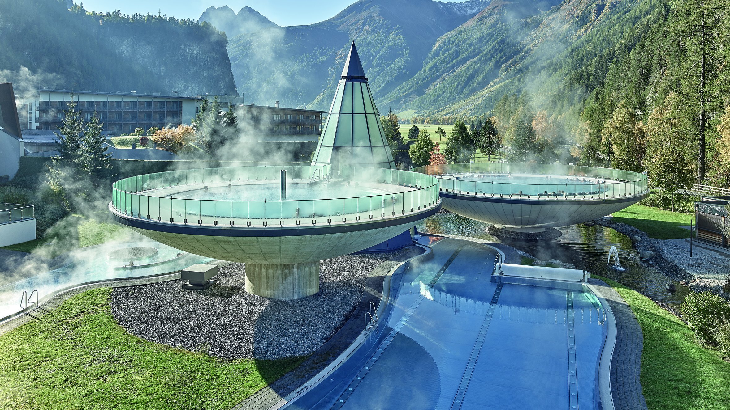 Moderne Therme im Alpenland Kreisförmige Thermalbecken und ein Außenpool in Berglandschaft mit klarem Himmel
