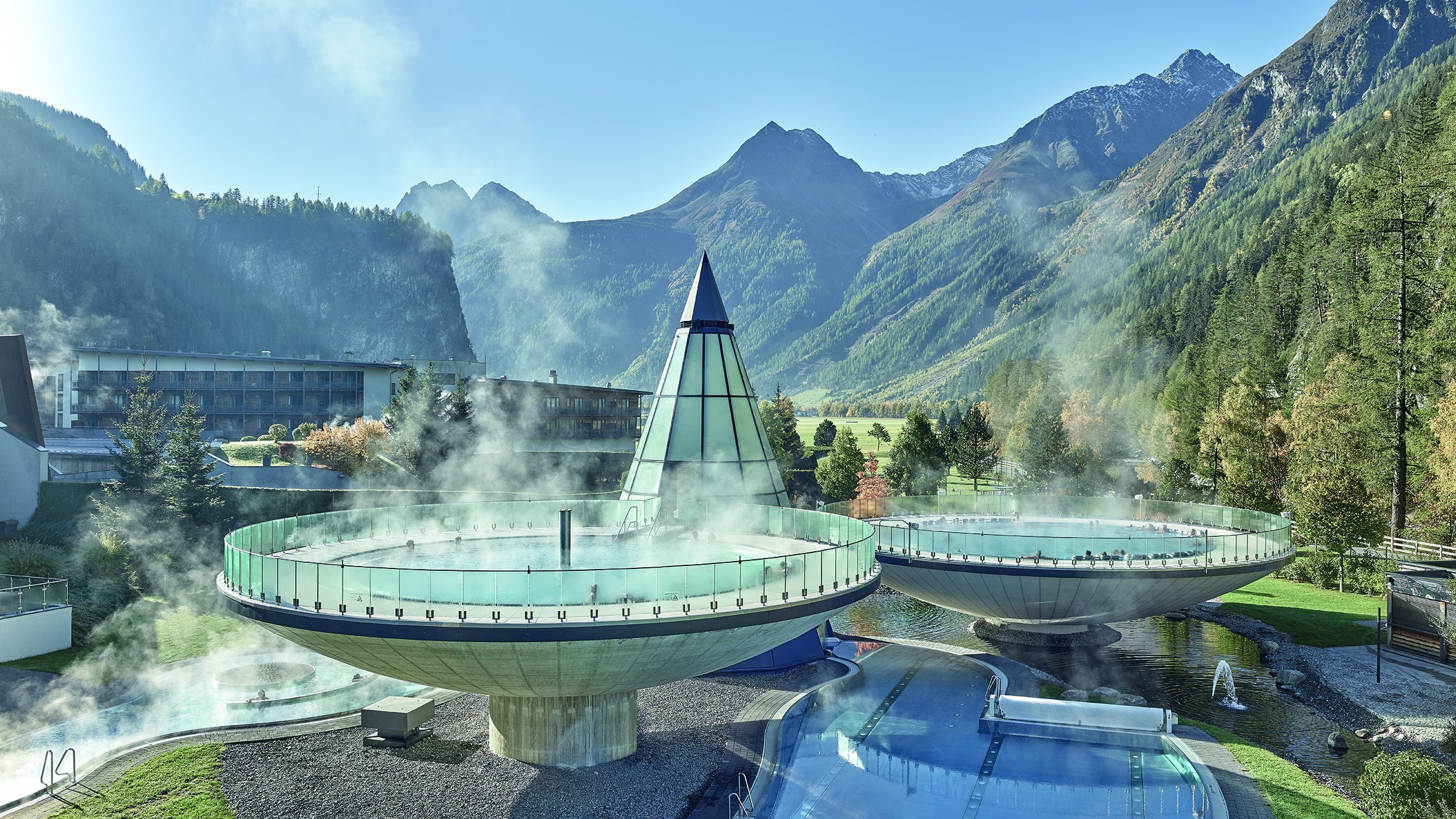 Moderne Therme im Alpenland Kreisförmige Thermalbecken und ein Außenpool in Berglandschaft mit klarem Himmel
