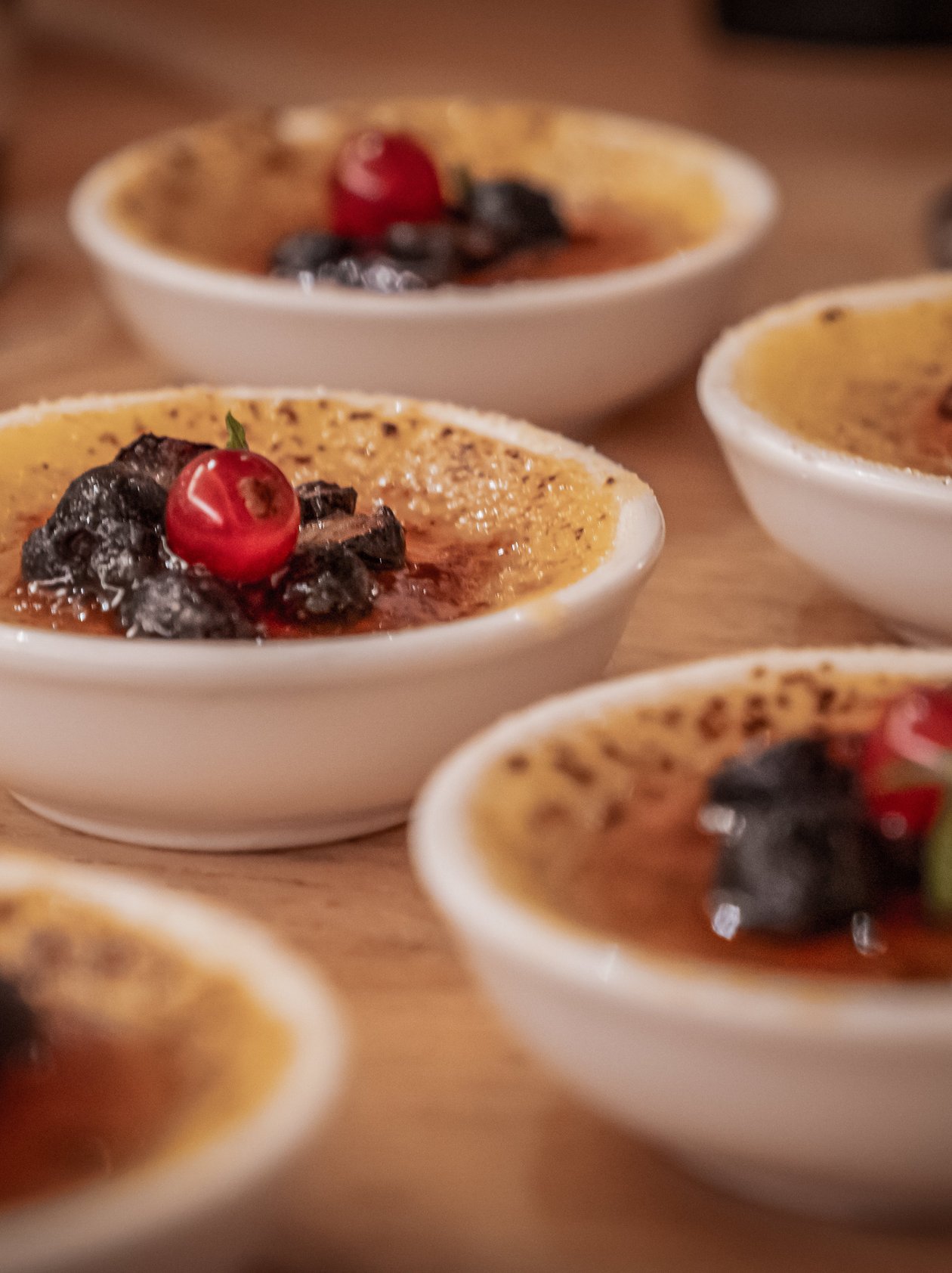 Small bowls of creme brulee topped with black ingredients and garnished with red berries.