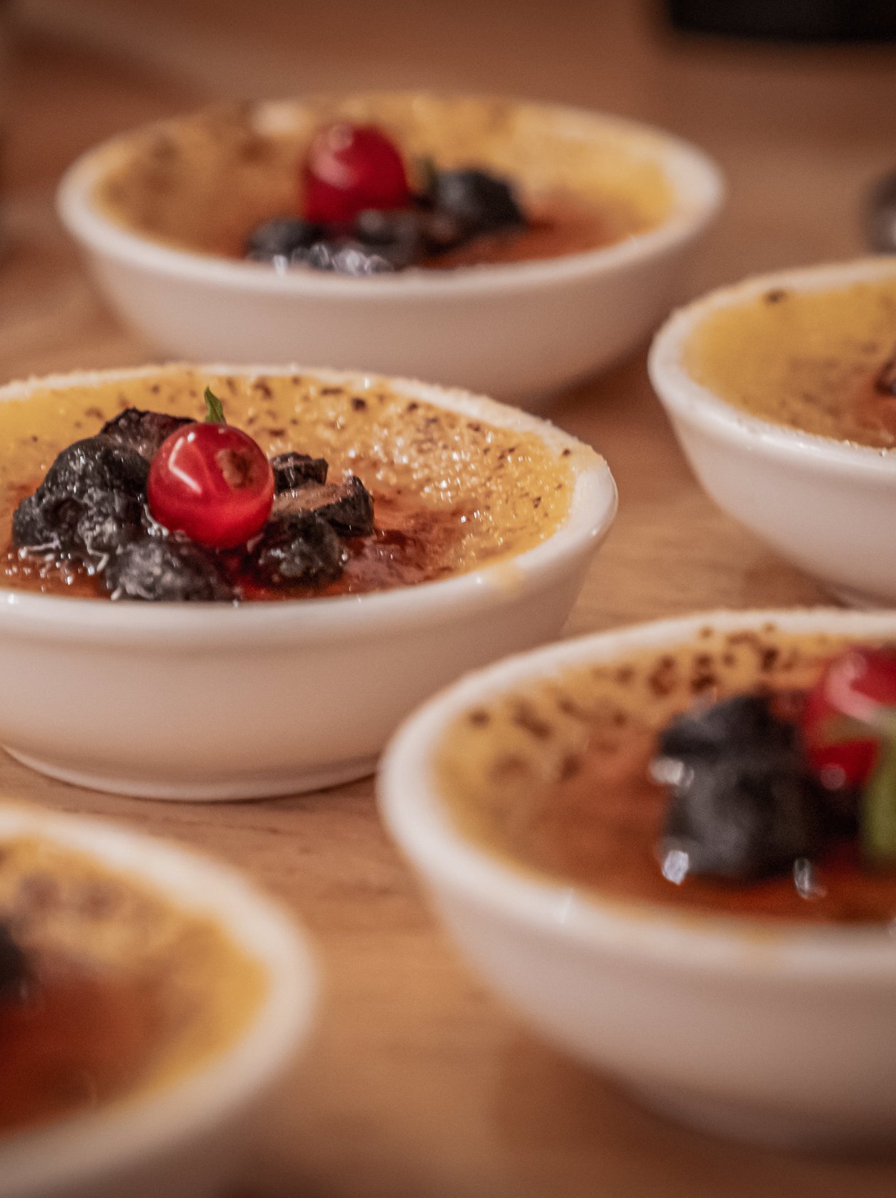 Mehrere kleine Dessertschalen mit Creme Brulee, garniert mit roten Beeren und dunklen Zutaten.