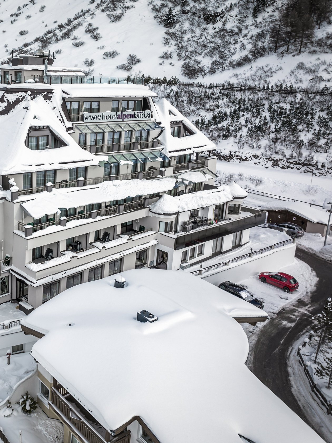 Großes Gebäude in den Bergen, umgeben von schneebedeckten Bäumen und Pisten im Winter.