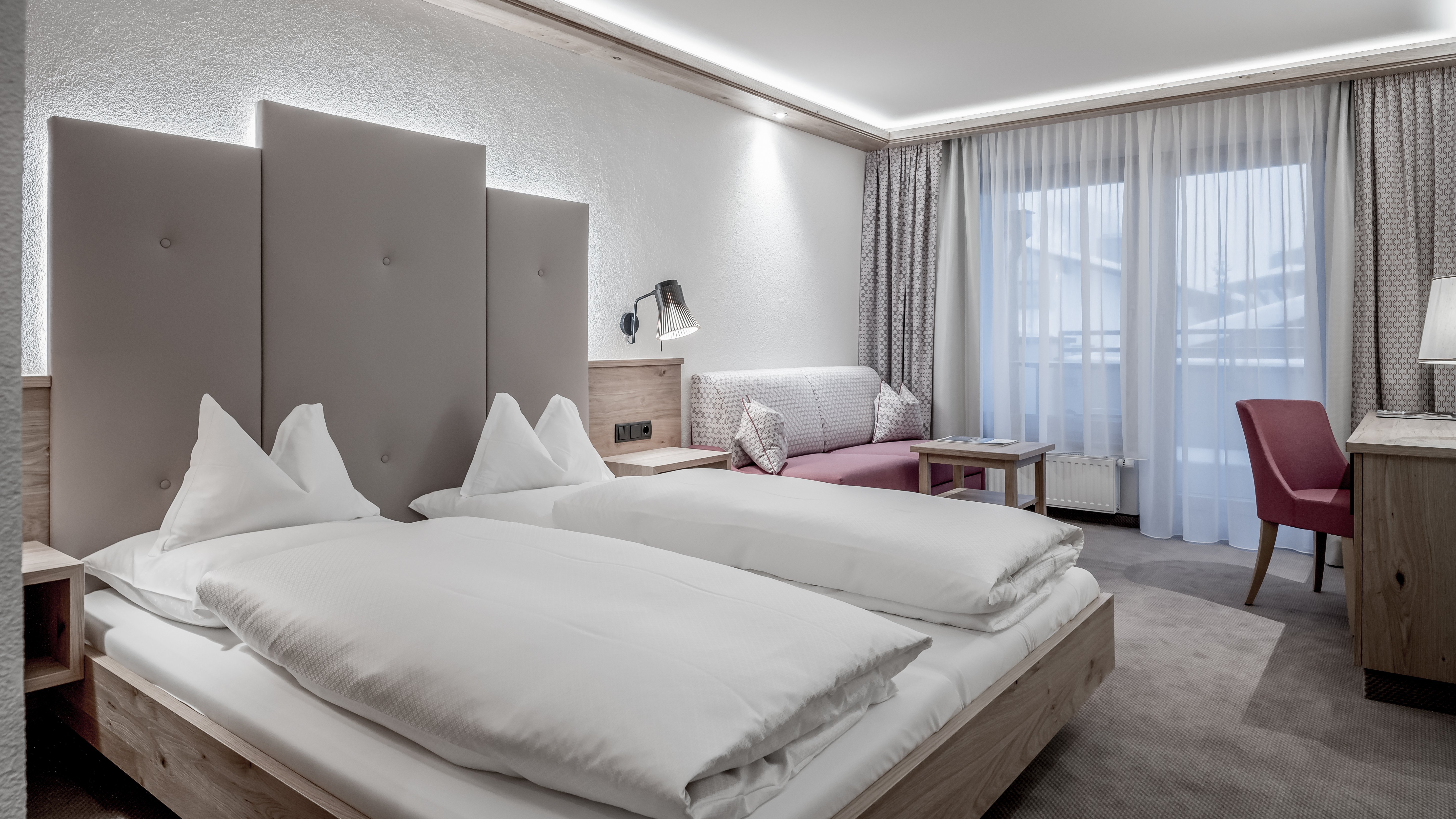 Moderne Hotelzimmer im Alpenland Zwei Einzelbetten in einem modernen Hotelzimmer mit Sitzecke und großen Fenstern.