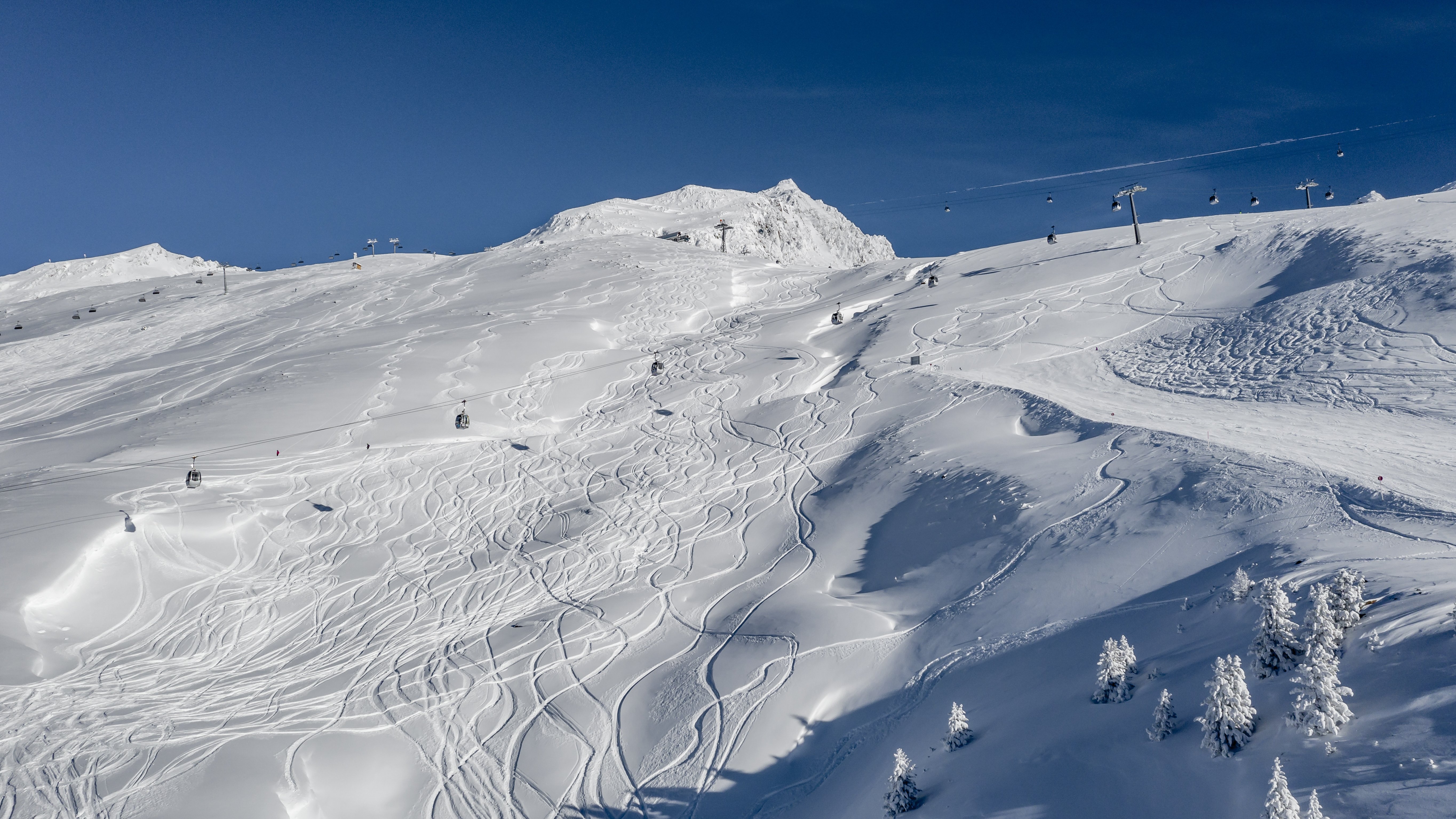 Winteridylle im Skigebiet Verschneite Berglandschaft mit Skispuren und Skiliften unter blauem Himmel. Einfacher Zugang zu den Pisten.