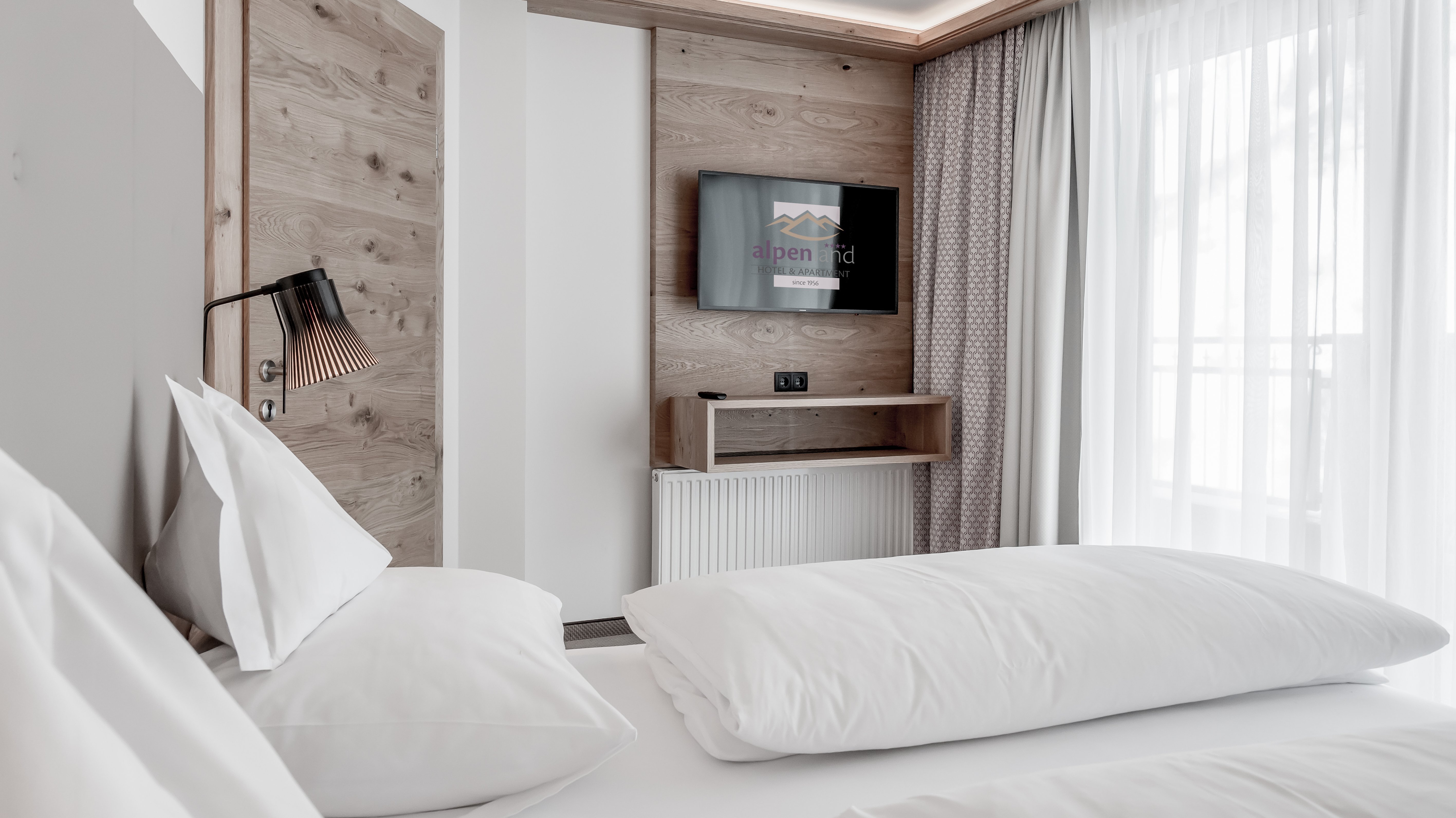 Hotelzimmer mit Bett, Holzwand und montiertem Fernseher in minimalistischen Stil.