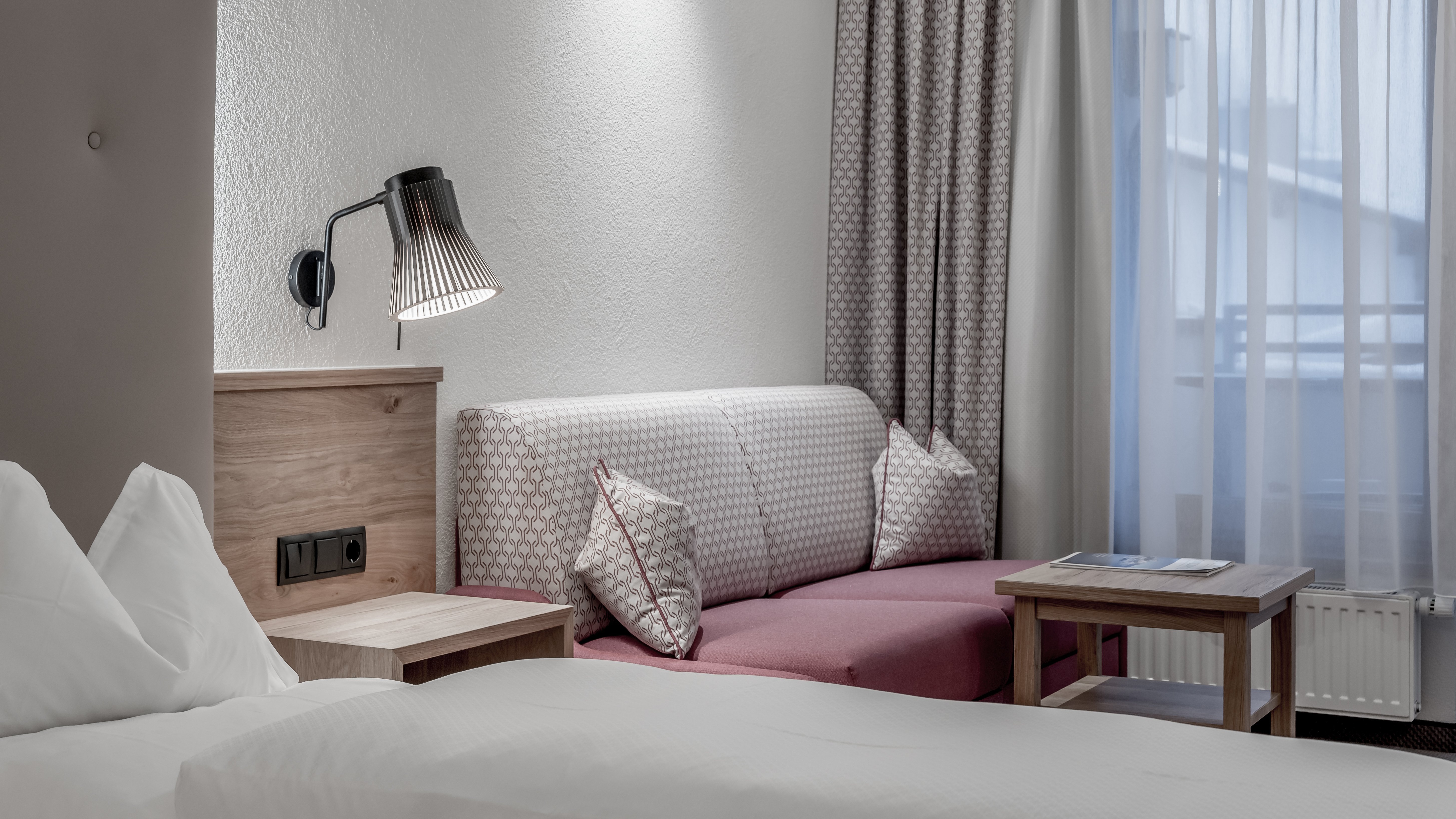 Moderne Hotelzimmer mit Komfort Helles Hotelzimmer mit Bett, Sofa und Tisch im natürlichen Licht von einem Fenster.