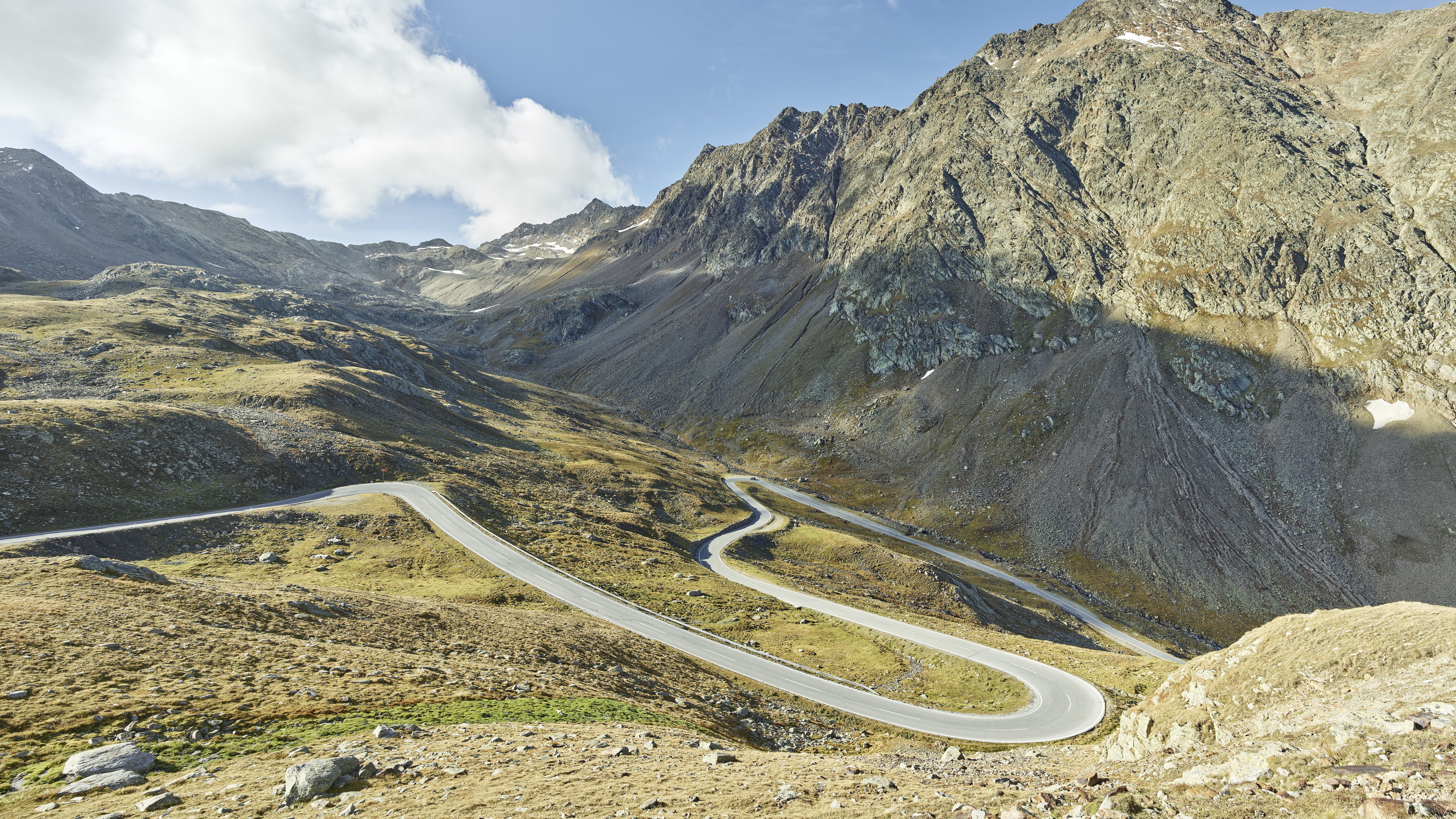 Schöne Alpenstraße im Ötztal Eine kurvenreiche Bergstraße, die sich durch eine grüne Landschaft schlängelt, darüber ein bewölkter Himmel und im Hintergrund Berge.