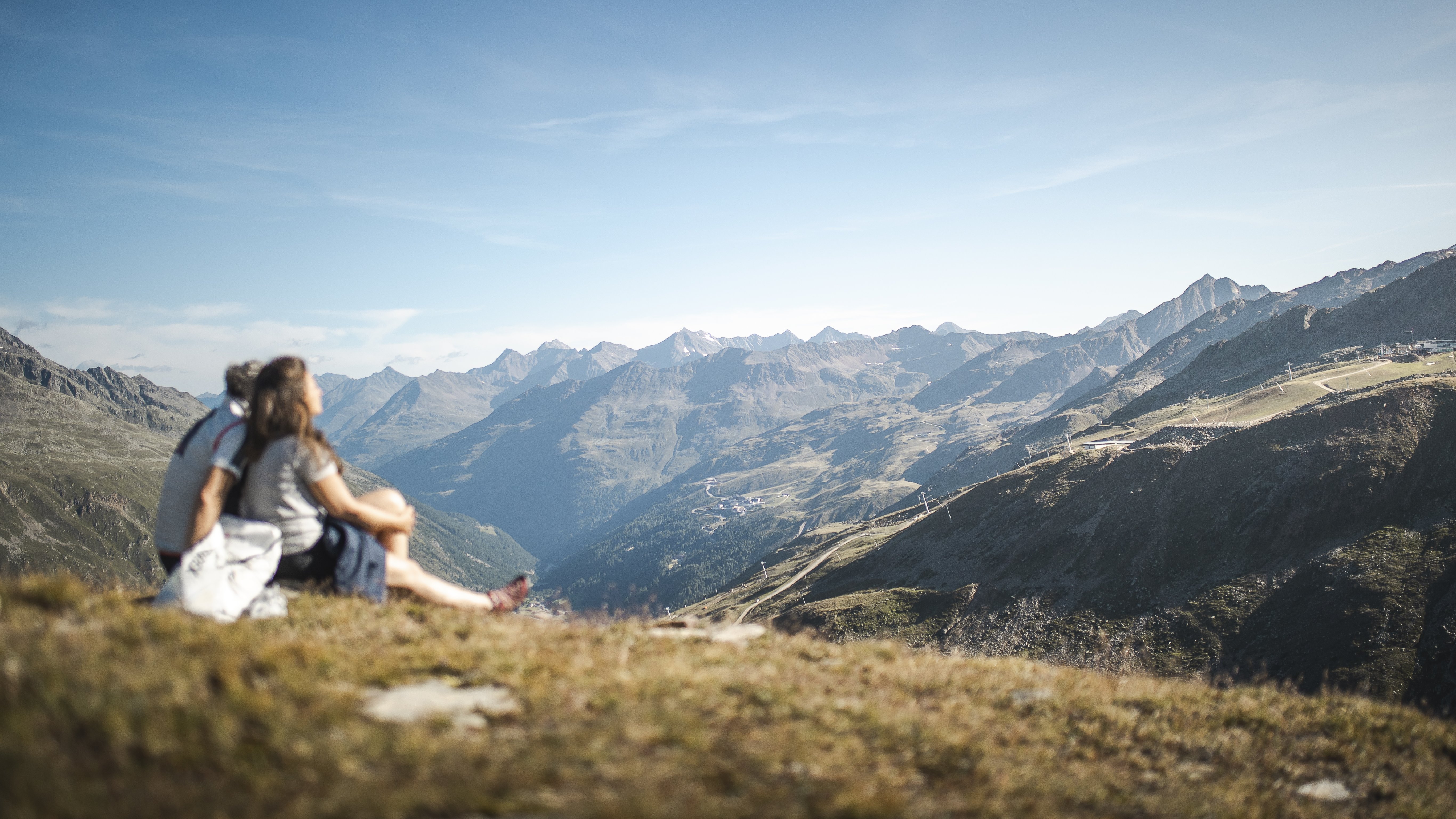 Romantische Auszeit in den Bergen Ein Paar sitzt auf einer Wiese und genießt die Aussicht auf die Berglandschaft unter blauem Himmel.