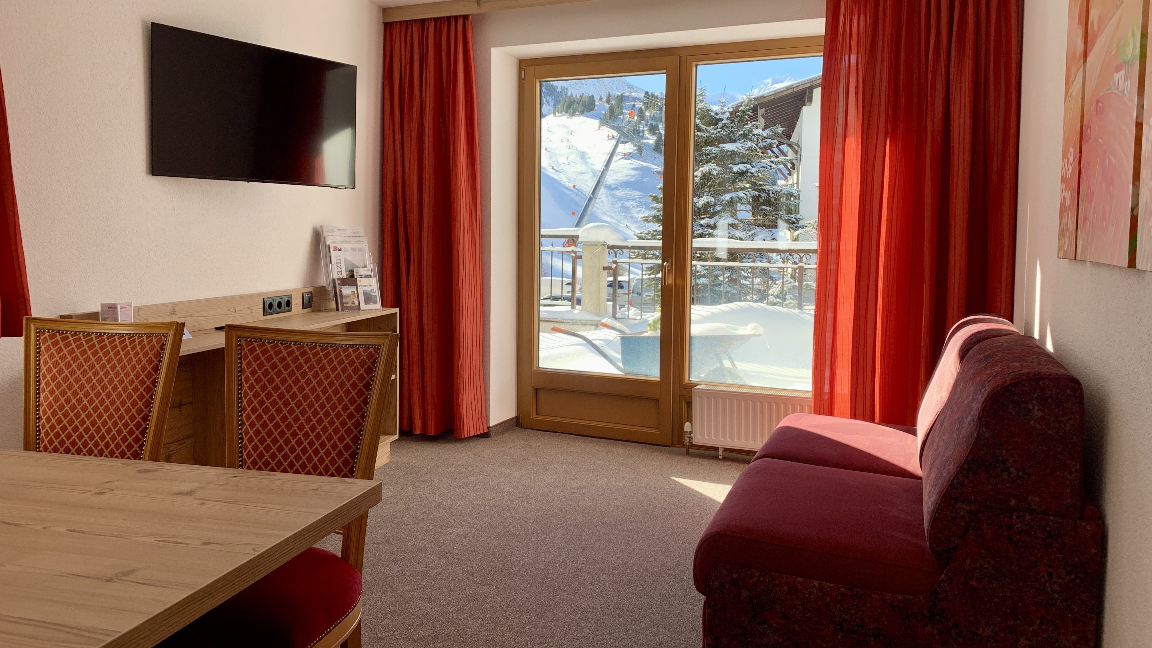 Gemütlicher Rückzugsort mit Bergblick Hotelzimmer mit Sitzbereich, Holzschreibtisch und großen Fenstern zur Berglandschaft.
