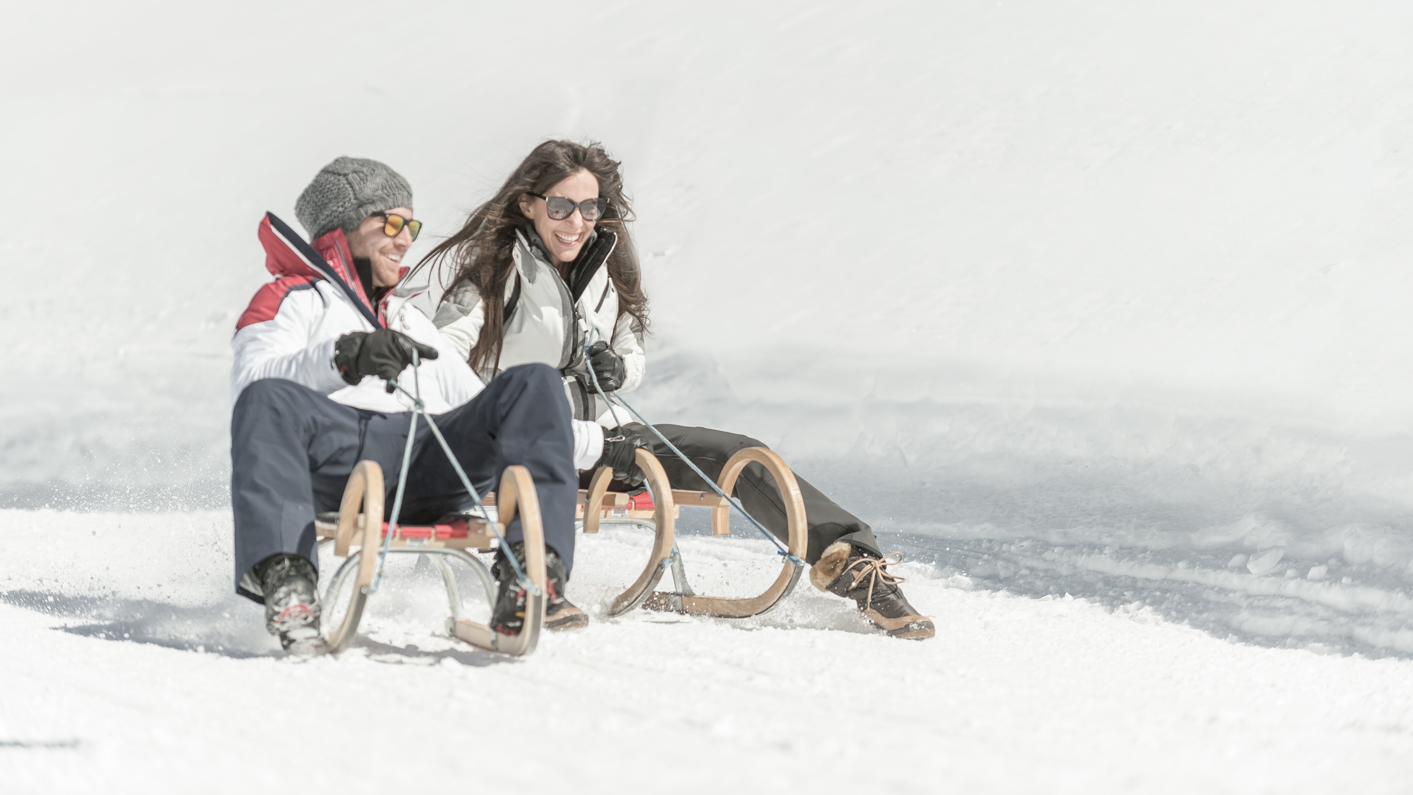 Paar fährt fröhlich auf einem Schlitten eine verschneite Piste hinunter und genießt den Winter.