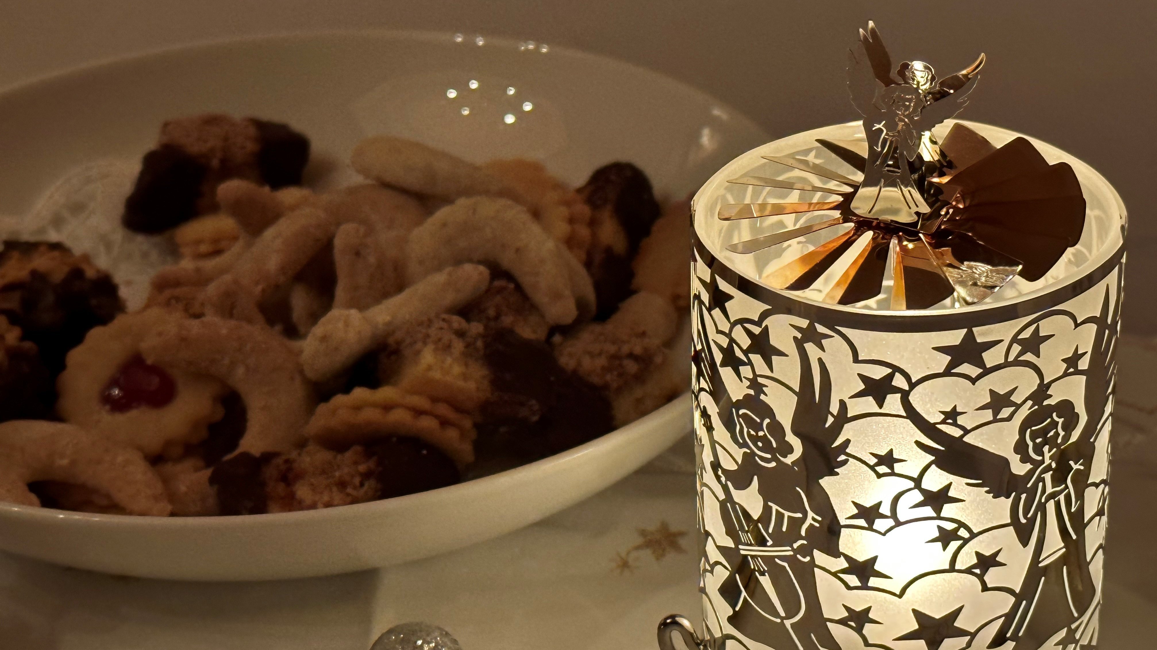 Dekorative Lampe mit Engel und Teller voller Kekse auf einem Tisch mit Weihnachtsdeko.