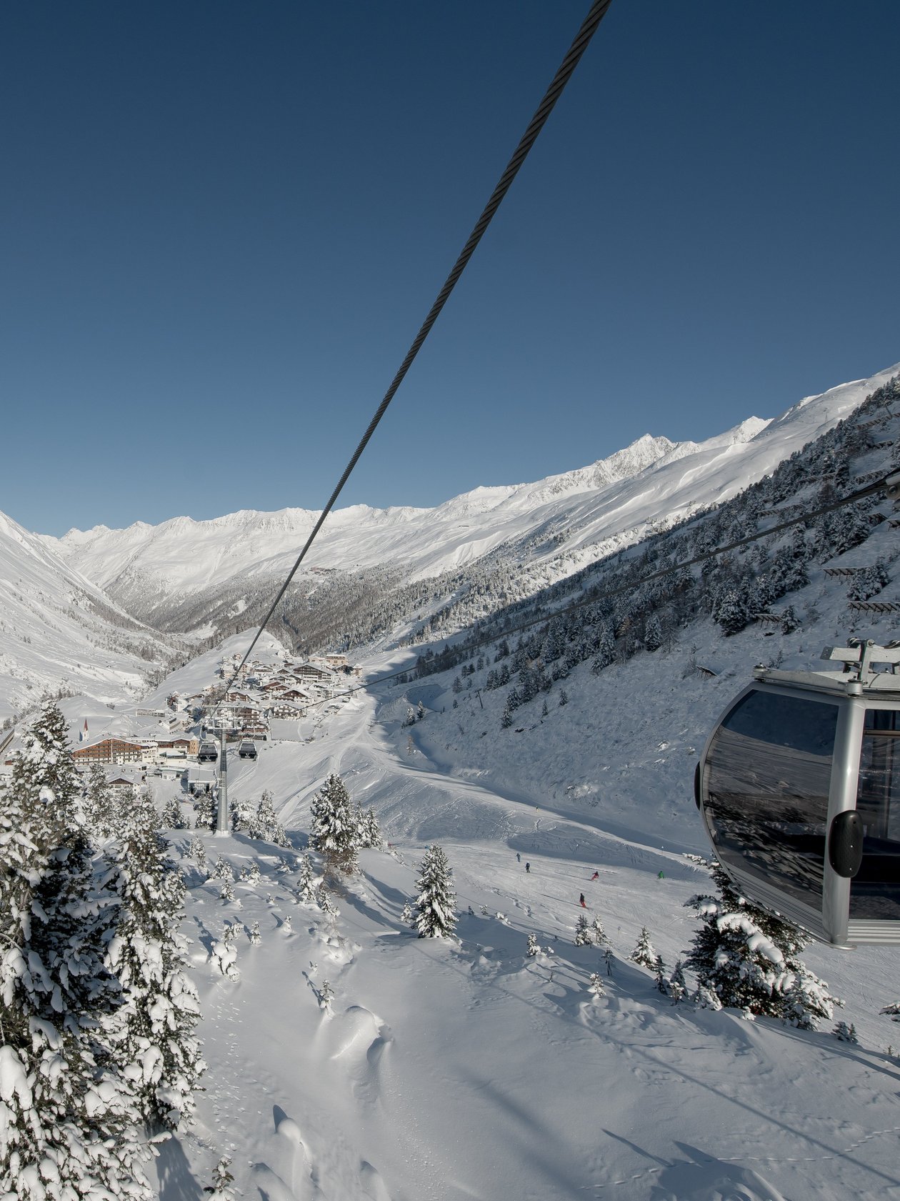 Seilbahn über schneebedeckte Berge Seilbahn fährt über verschneite Landschaft mit Bergen und kleinem Dorf im Hintergrund