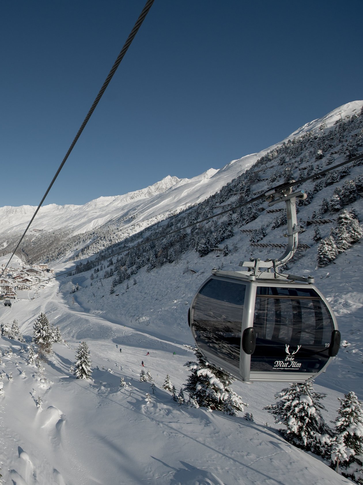 Seilbahn fährt über verschneite Landschaft mit Bergen und kleinem Dorf im Hintergrund