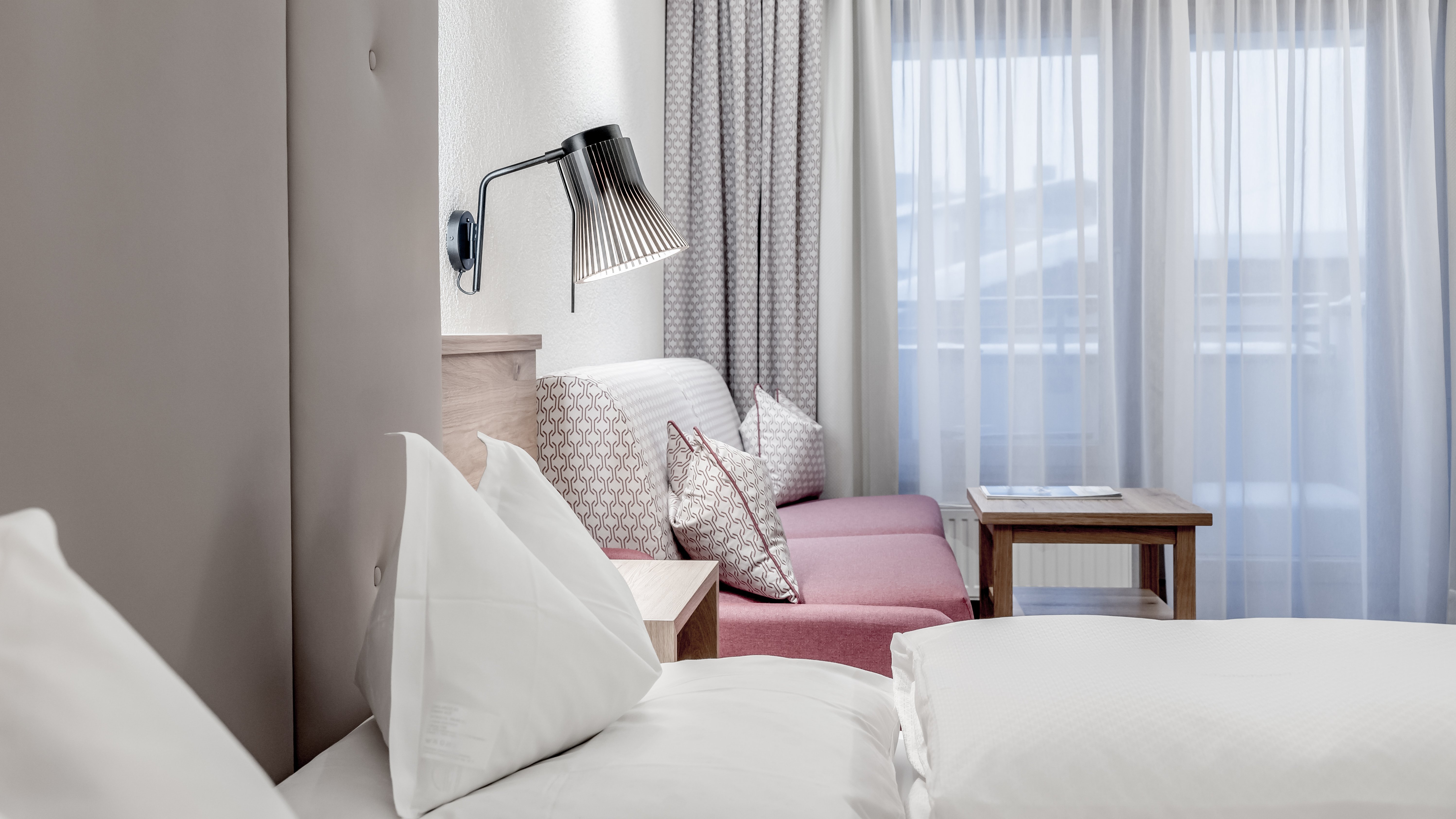 Modernes Hotelzimmer mit gemütlichem Design Helles Hotelzimmer mit einem Bett, einer Couch und großen Fenstern mit transparenten Vorhängen.