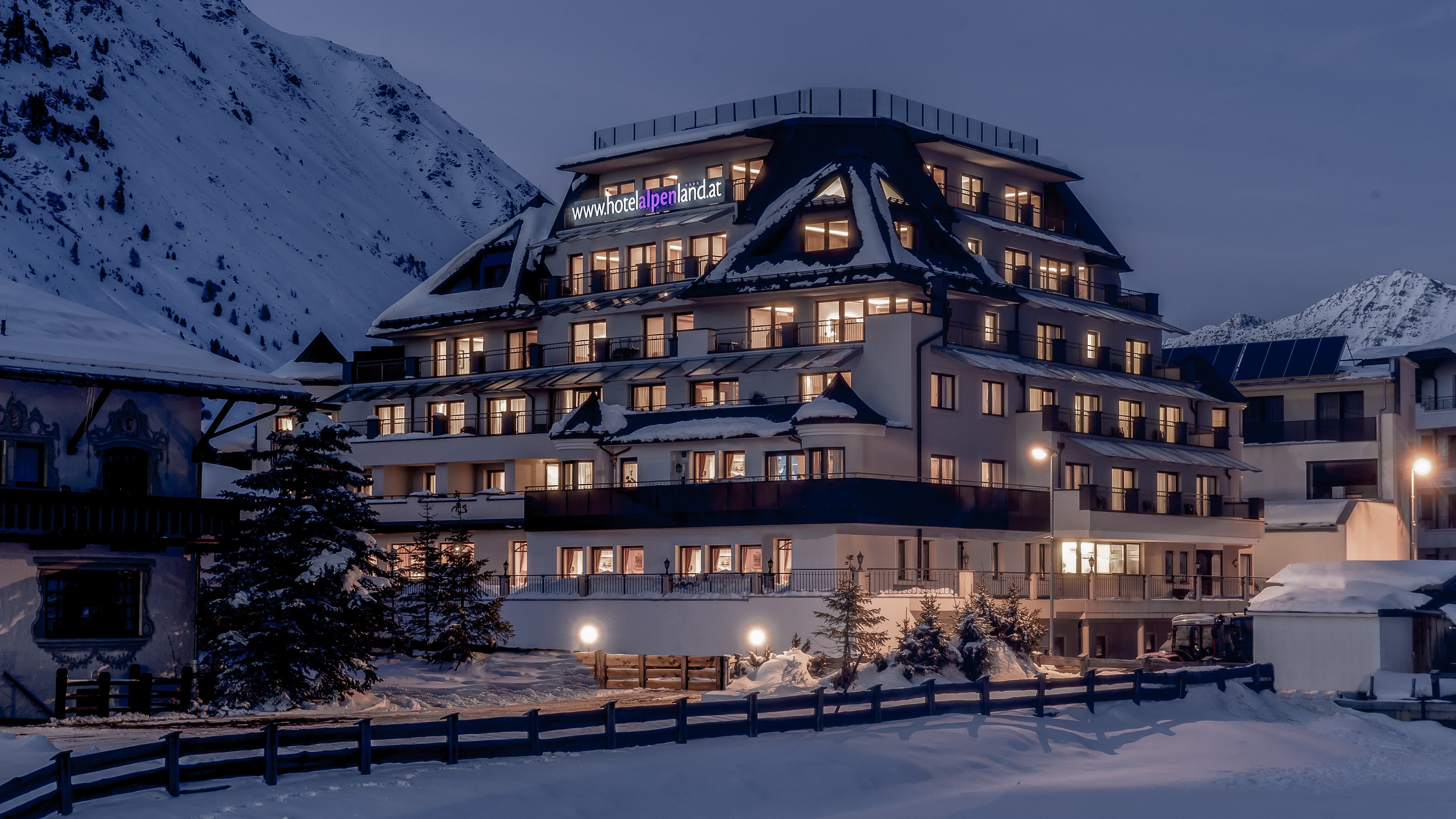 Mehrstöckiges Hotelgebäude in einer verschneiten Berglandschaft bei Dämmerung.